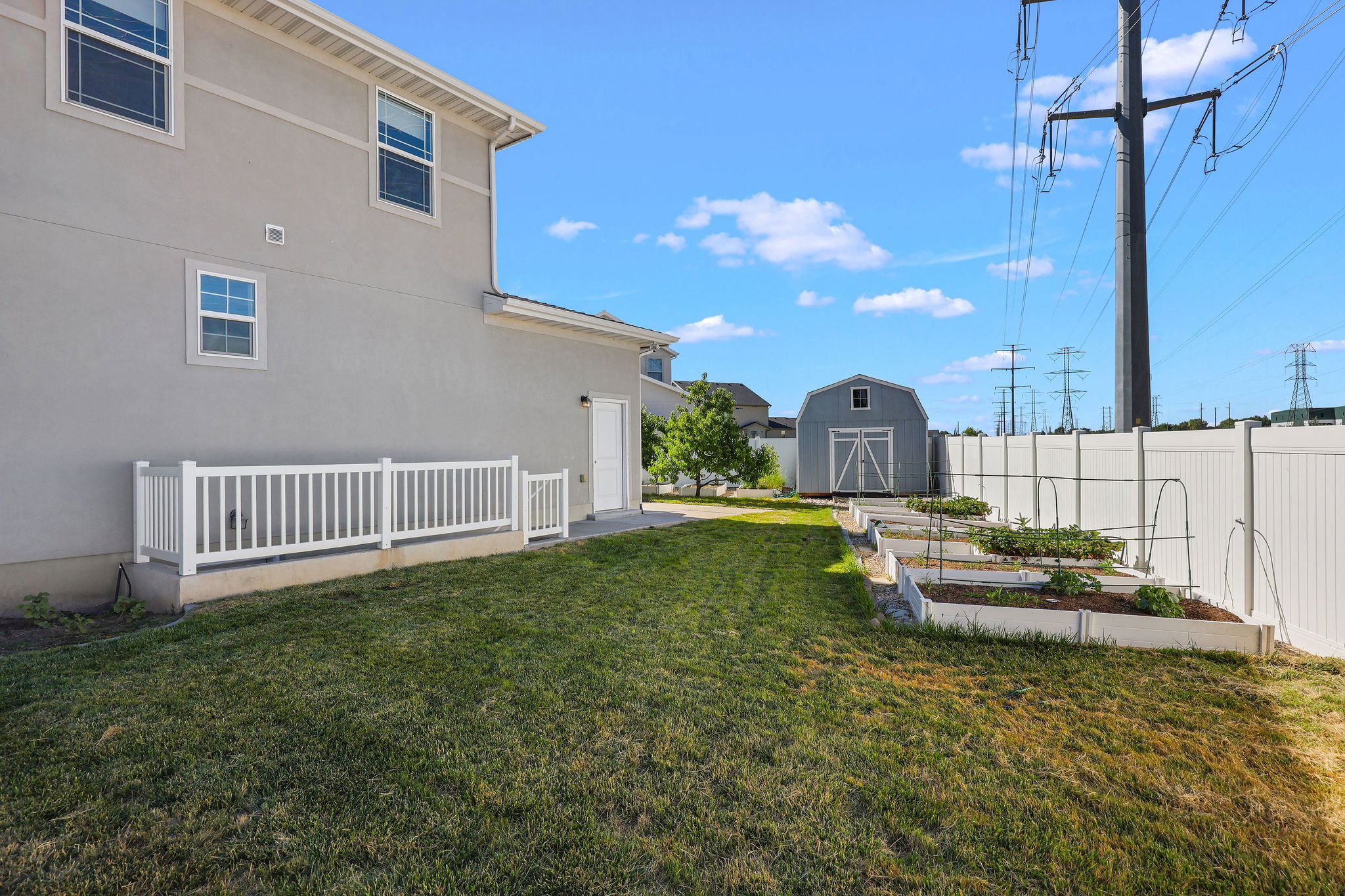 Spacious backyard featuring a manicured lawn, white vinyl fencing, a detached storage shed, and multiple raised garden beds