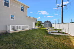 Spacious backyard featuring a manicured lawn, white vinyl fencing, a detached storage shed, and multiple raised garden beds
