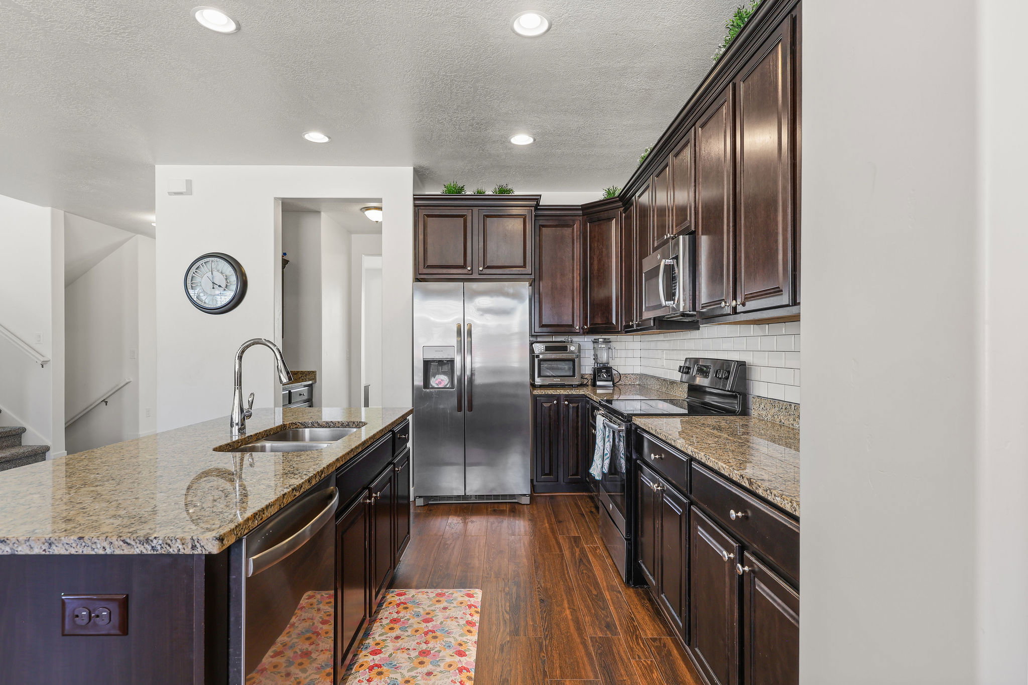 Modern kitchen featuring dark wood cabinetry, stainless steel appliances, granite countertops, wood-finish flooring, and recessed lighting