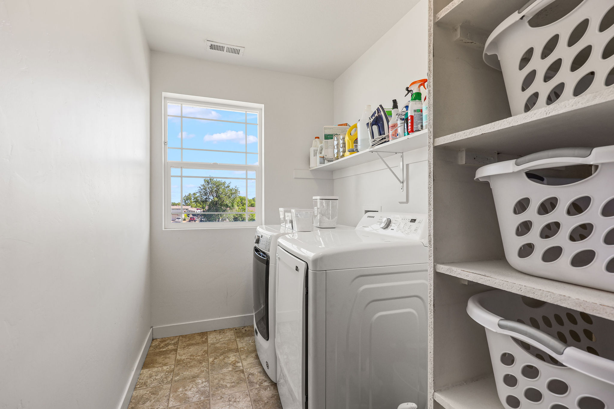 Dedicated laundry area featuring a window, built-in shelving, a wall-mounted shelf, and tile-finish flooring