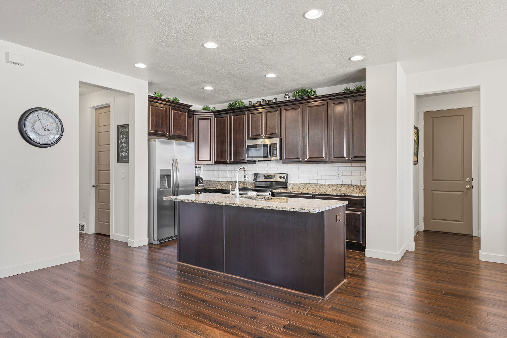 Kitchen featuring dark wood cabinetry, stainless steel appliances, a subway tile backsplash, and an island with a light-toned countertop