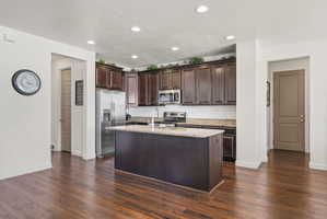 Kitchen featuring dark wood cabinetry, stainless steel appliances, a subway tile backsplash, and an island with a light-toned countertop
