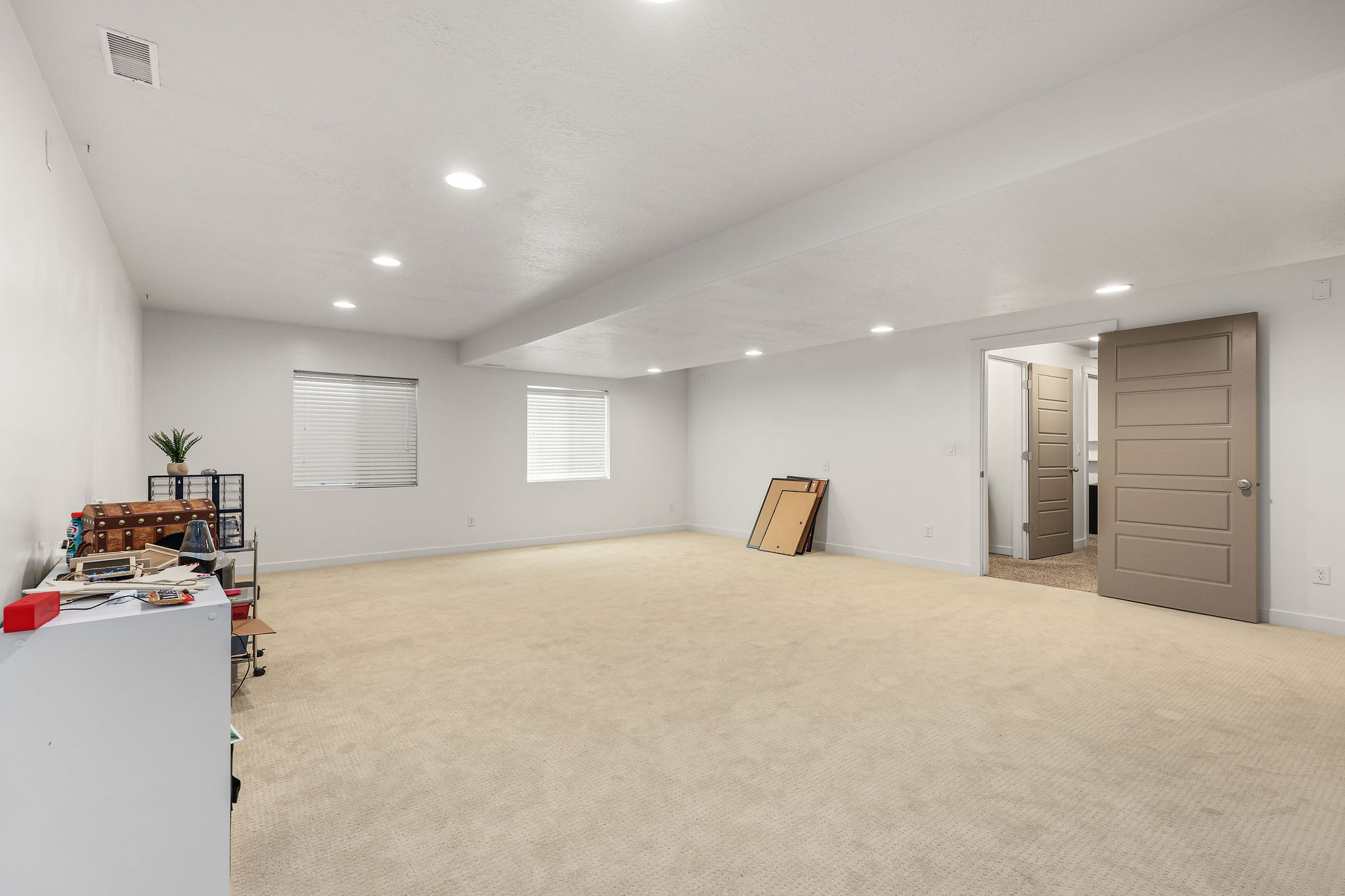Spacious carpeted room featuring recessed lighting, two windows with horizontal blinds, and a five-panel interior door