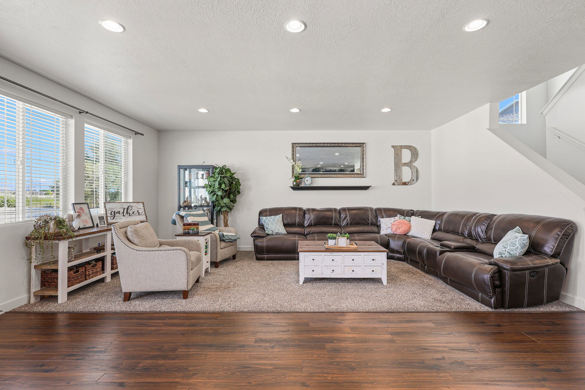 Open living area featuring wood-finish flooring transitioning to carpet, recessed lighting, and a prominent window array with blinds