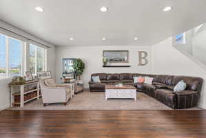 Open living area featuring wood-finish flooring transitioning to carpet, recessed lighting, and a prominent window array with blinds