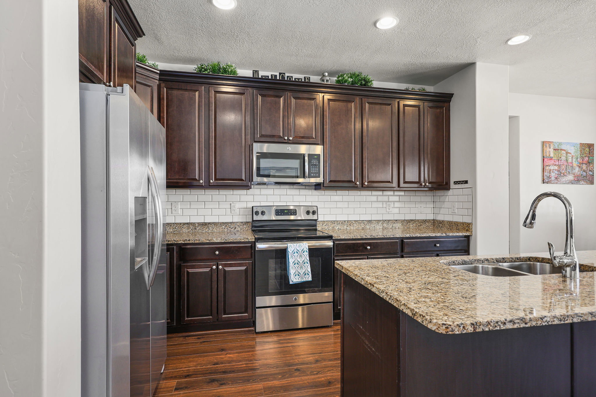 Kitchen featuring dark wood cabinetry, stainless steel appliances, a white subway tile backsplash, granite countertops, and wood-finish flooring