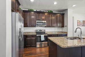 Kitchen featuring dark wood cabinetry, stainless steel appliances, a white subway tile backsplash, granite countertops, and wood-finish flooring