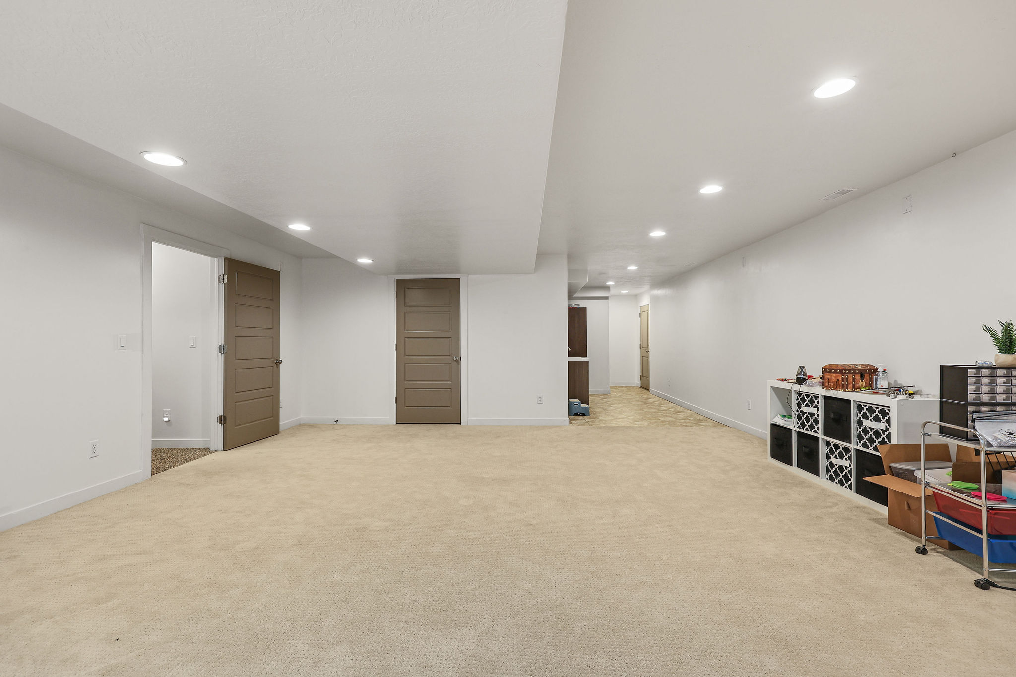 Expansive carpeted area with recessed lighting, white walls, and multiple panel doors