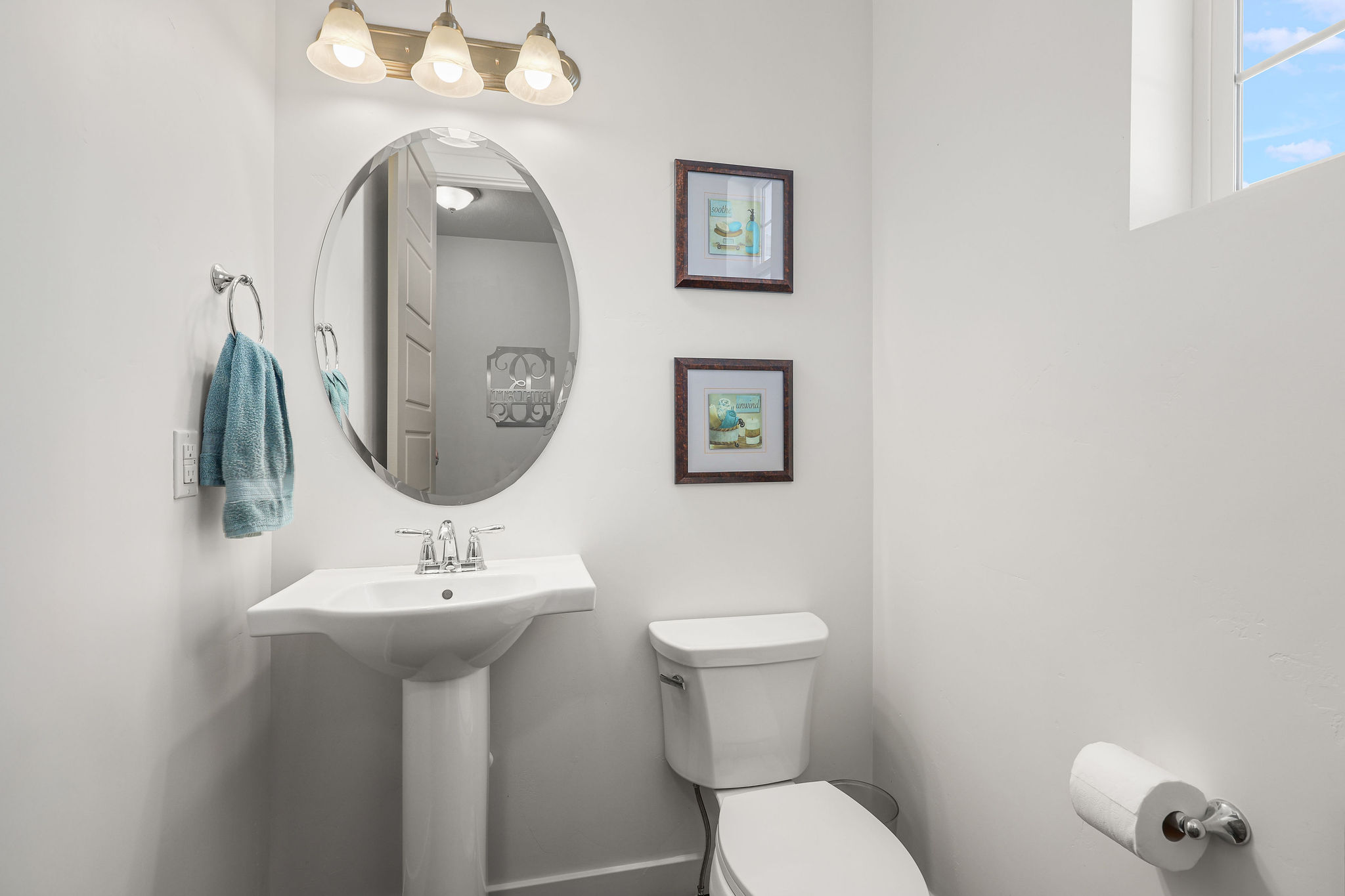 Pedestal sink with chrome faucet, oval mirror, and three-light vanity fixture