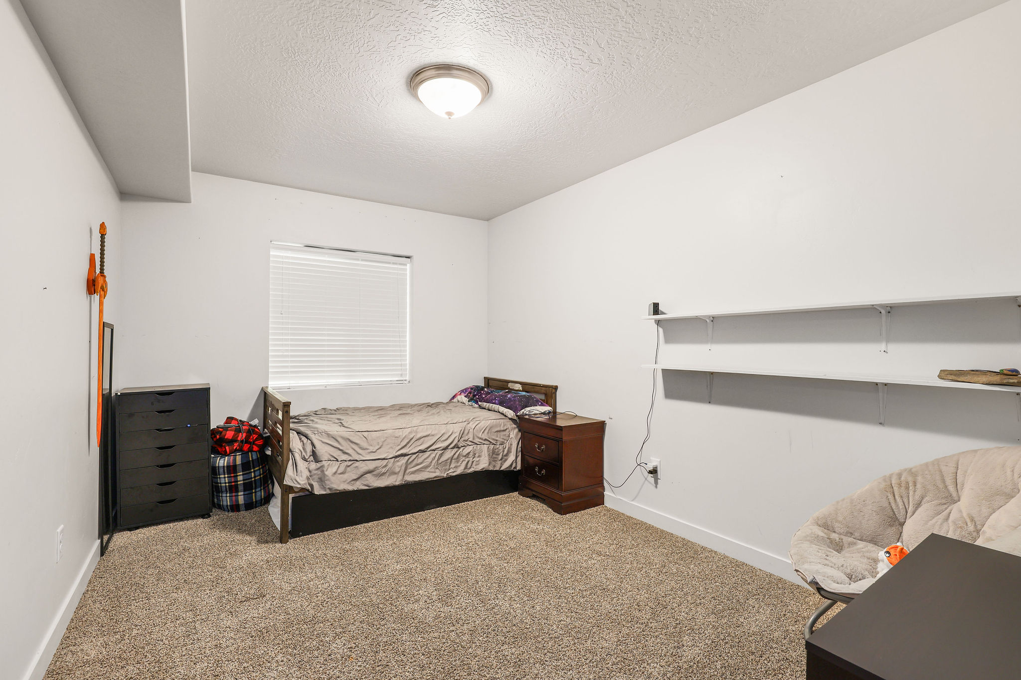 White walls, neutral carpet, and a window with blinds create a bright interior