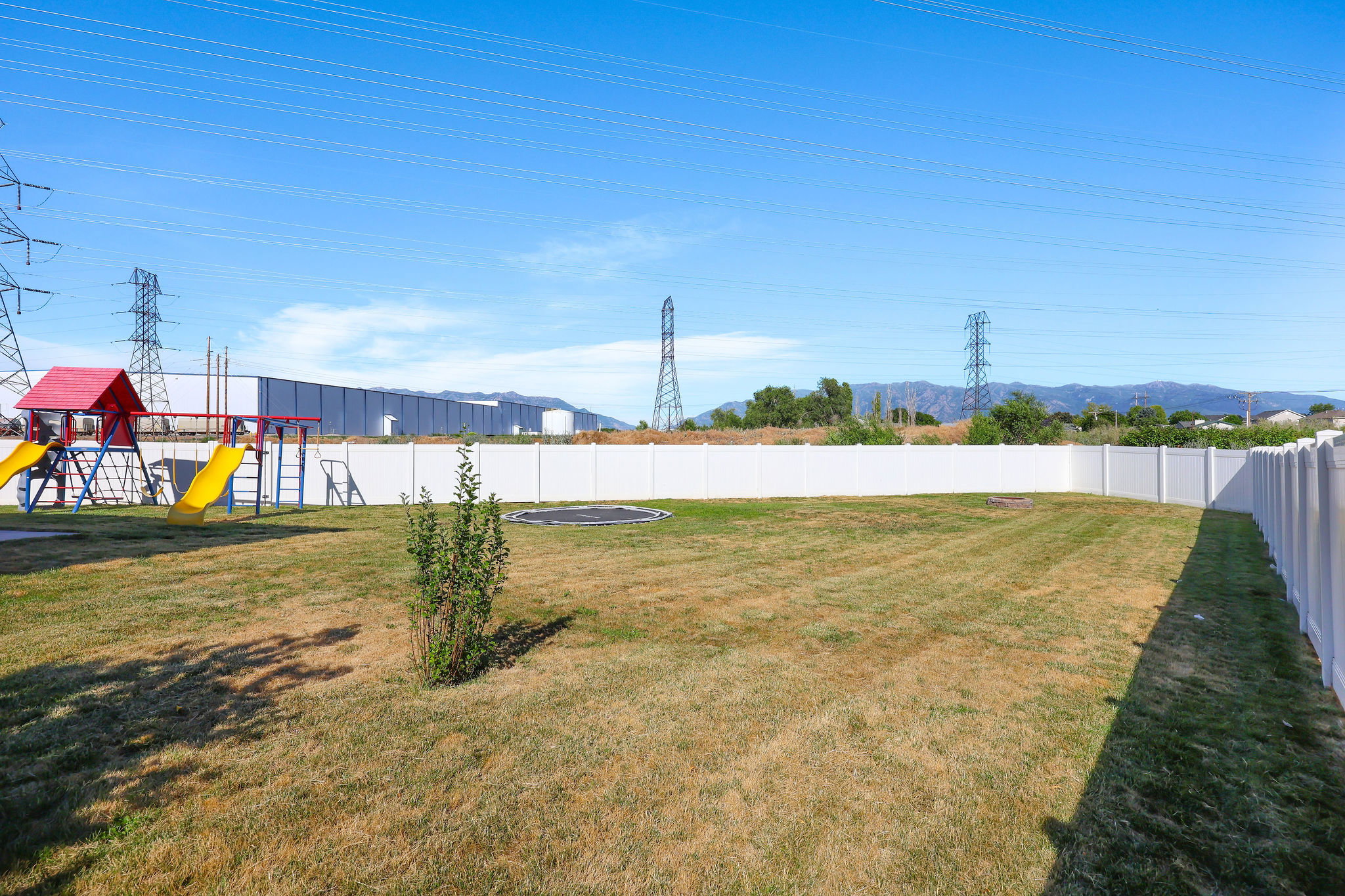 Expansive backyard featuring a white vinyl privacy fence, a swing set with slides, and a low-maintenance lawn