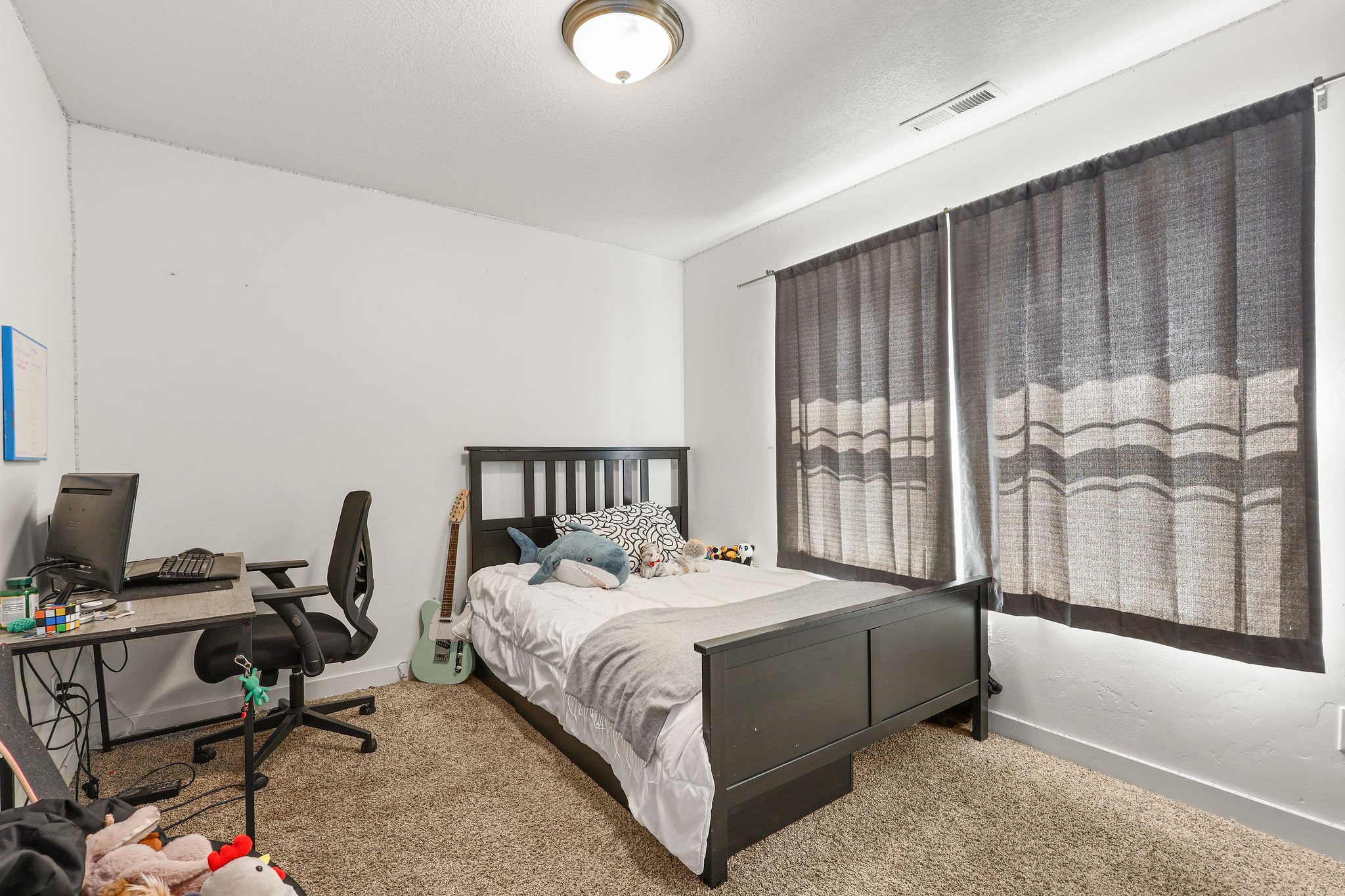 Carpeted bedroom with a built-in light fixture and two windows featuring dark drapery