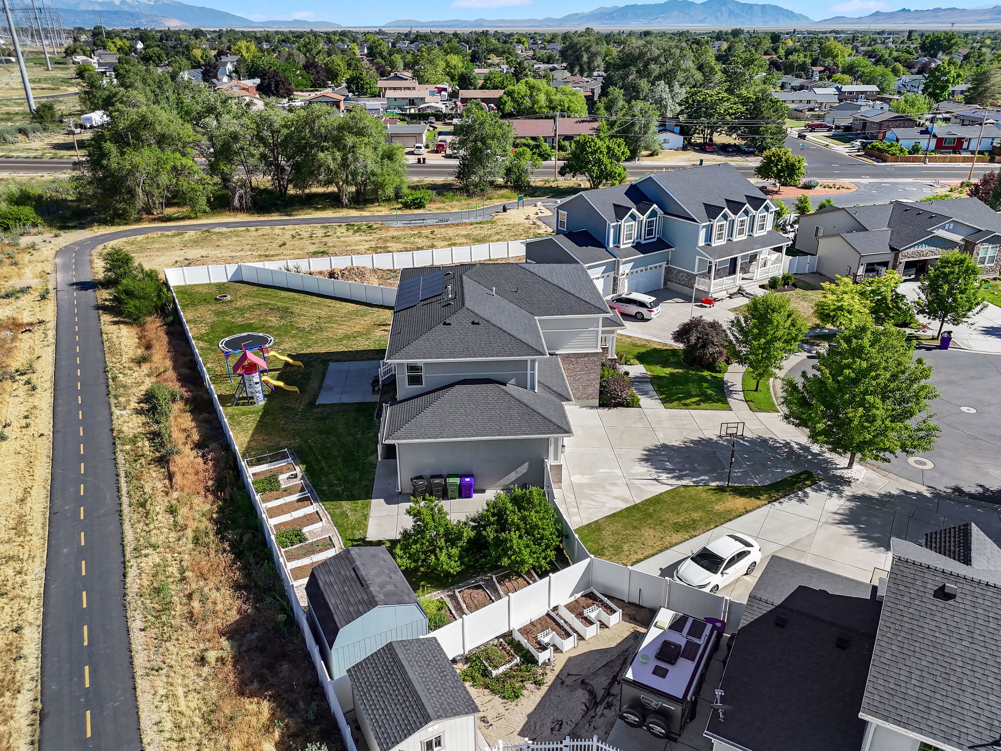 Aerial perspective showcasing a property with a spacious backyard, concrete patio, and a dedicated garden area with multiple raised beds