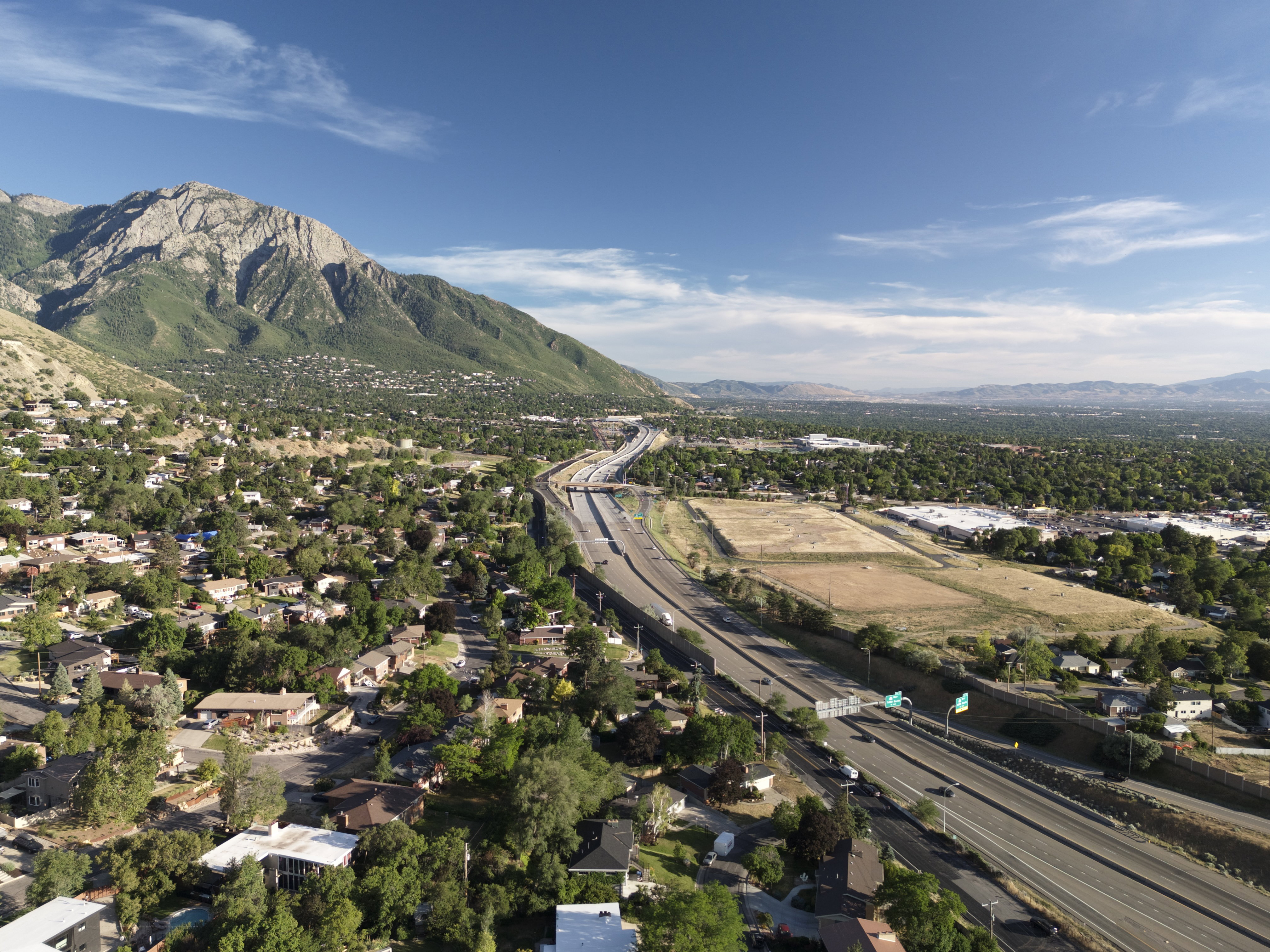 Aerial perspective showcasing a broad neighborhood with extensive tree cover, mountains, and a highway