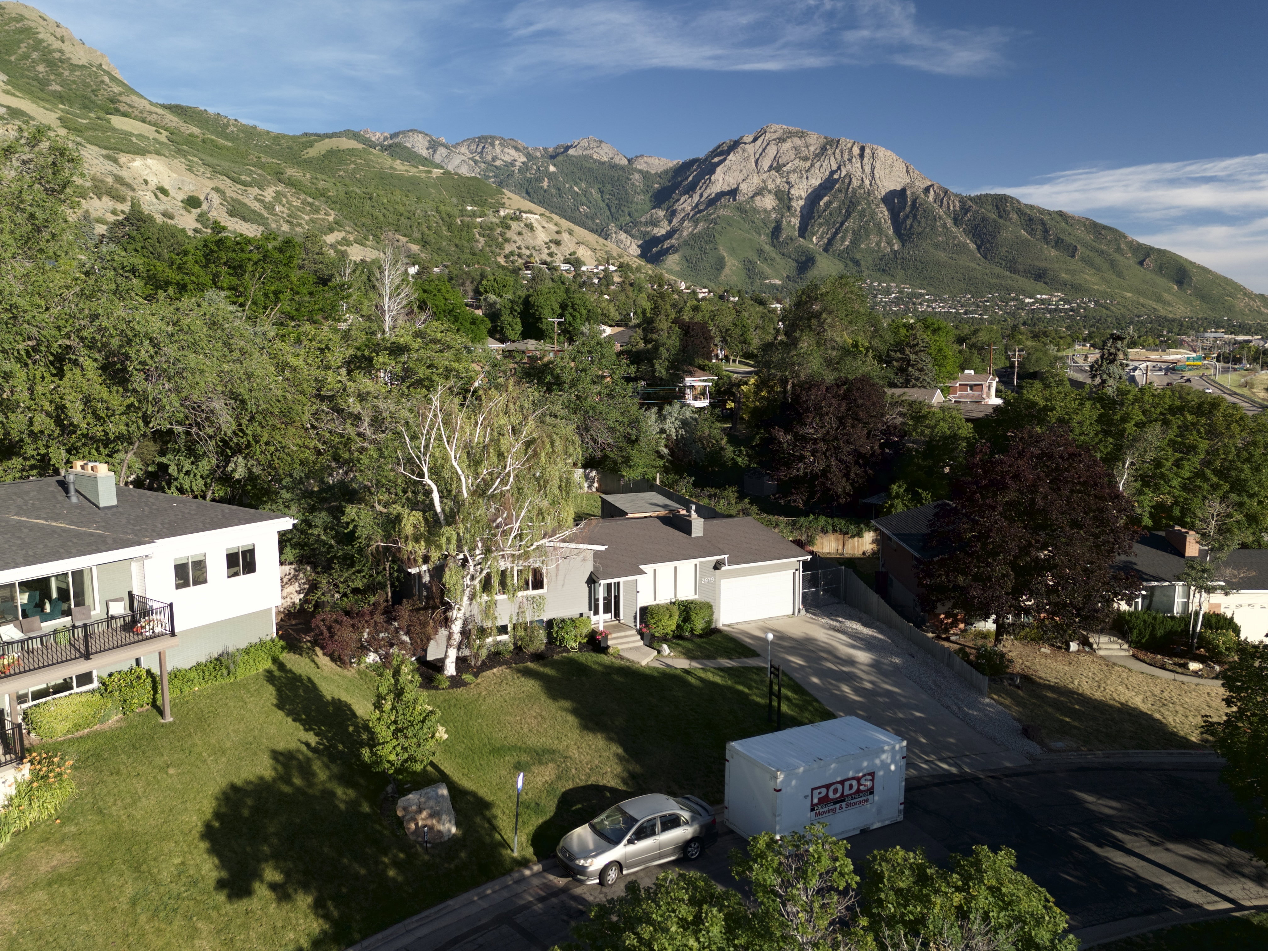 Property exterior featuring a mountain backdrop, mature trees, a driveway, and an attached garage