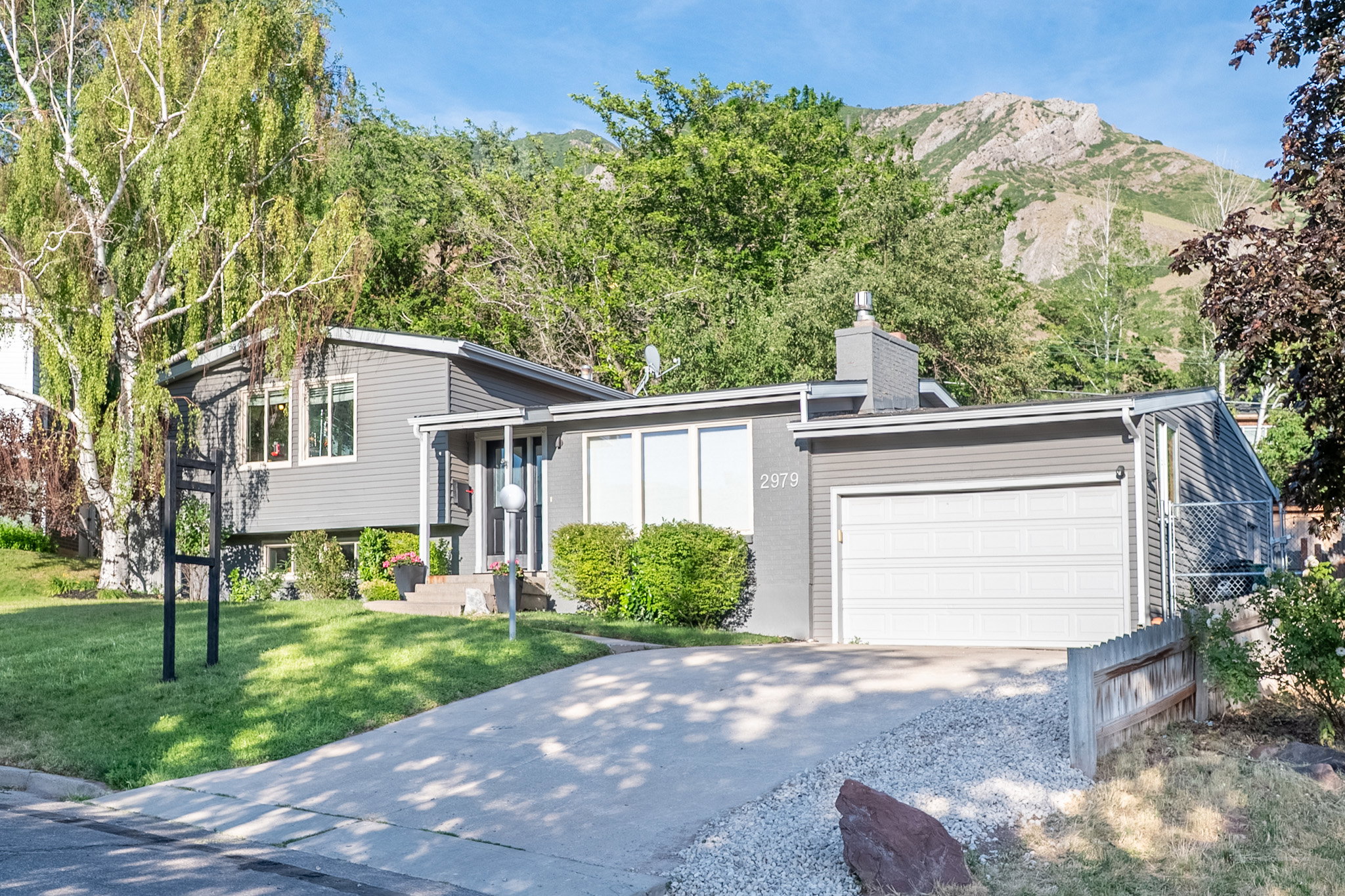 Mid-century modern residence featuring gray siding, a white garage door, and a concrete driveway