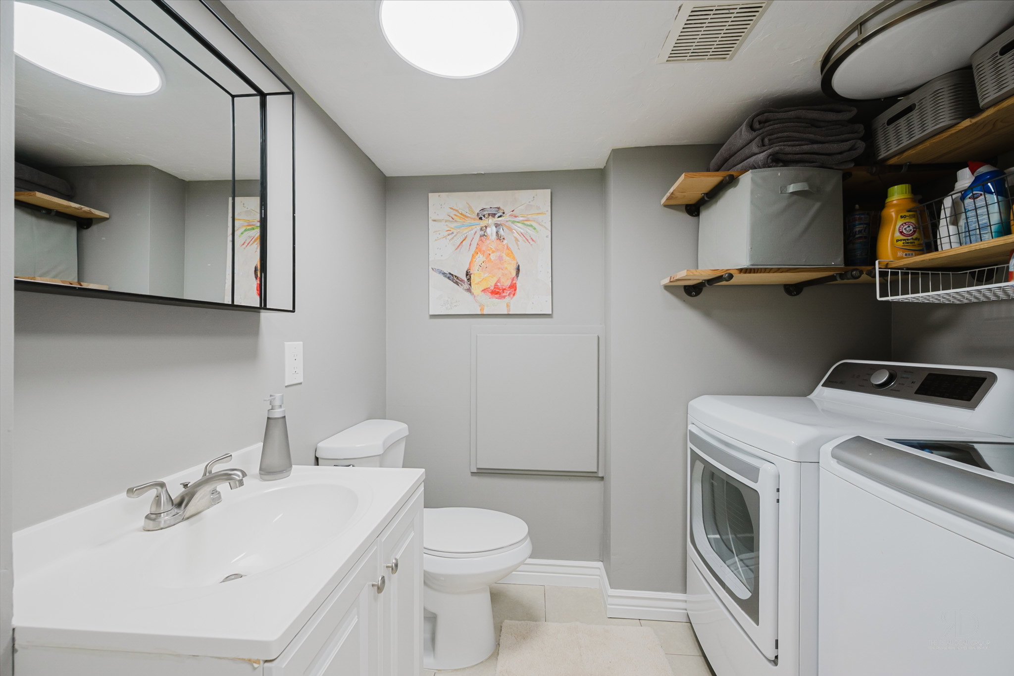 Utility room featuring a white vanity with integrated sink, a toilet, open wood shelving, and a side-by-side washer and dryer