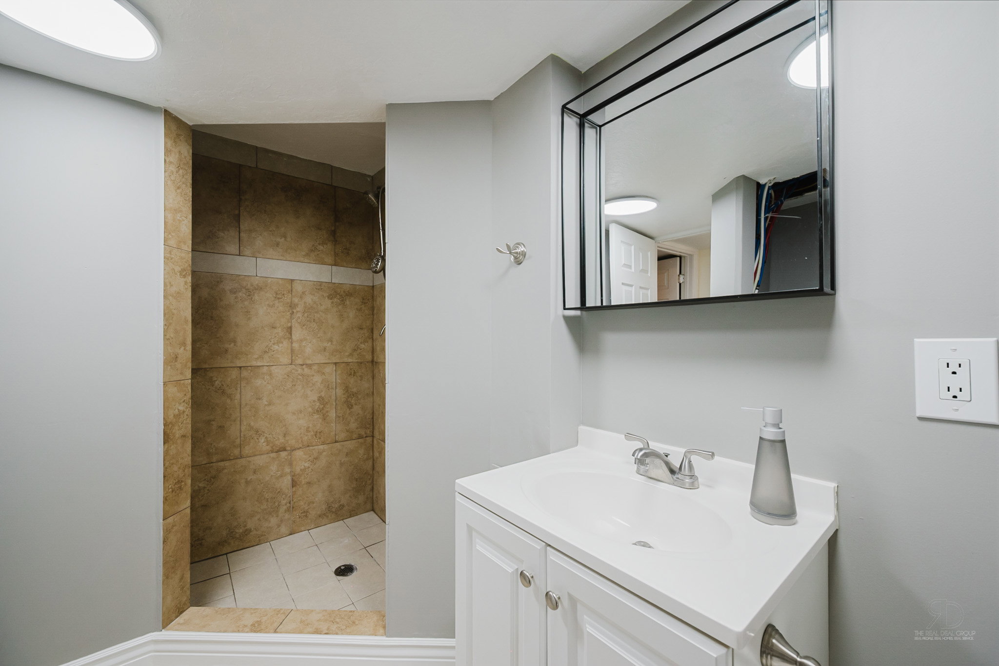 Bathroom featuring a stall shower with large format tile surround, a single vanity with storage, and a framed wall mirror