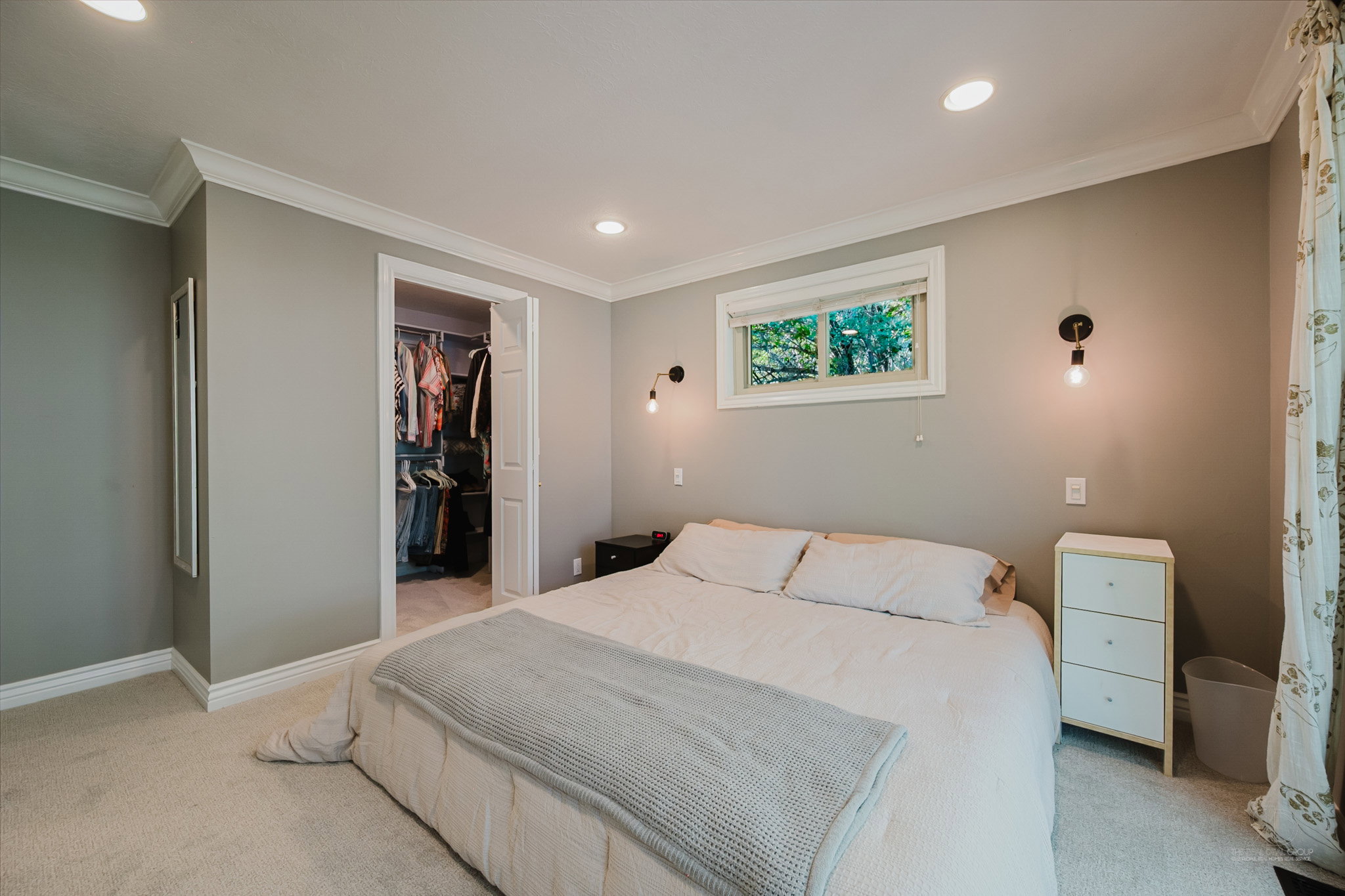 Spacious bedroom featuring light grey walls, recessed ceiling lights, crown molding, and a walk-in closet with built-in organization