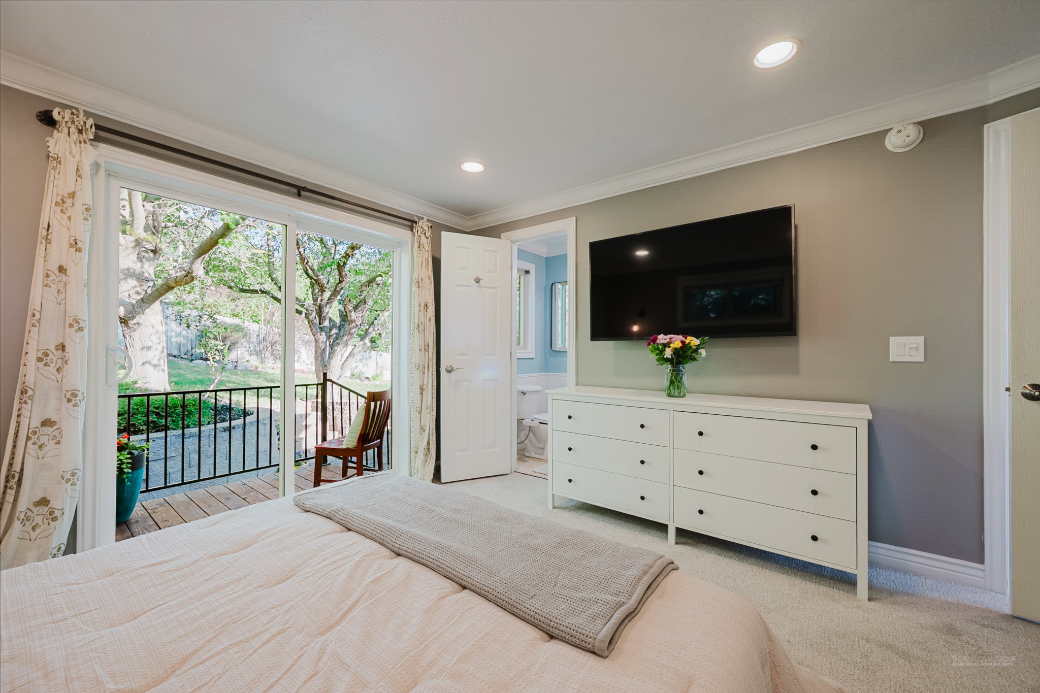 Carpeted bedroom with crown molding, recessed lighting, and a private balcony featuring a black metal railing and wood-finish decking
