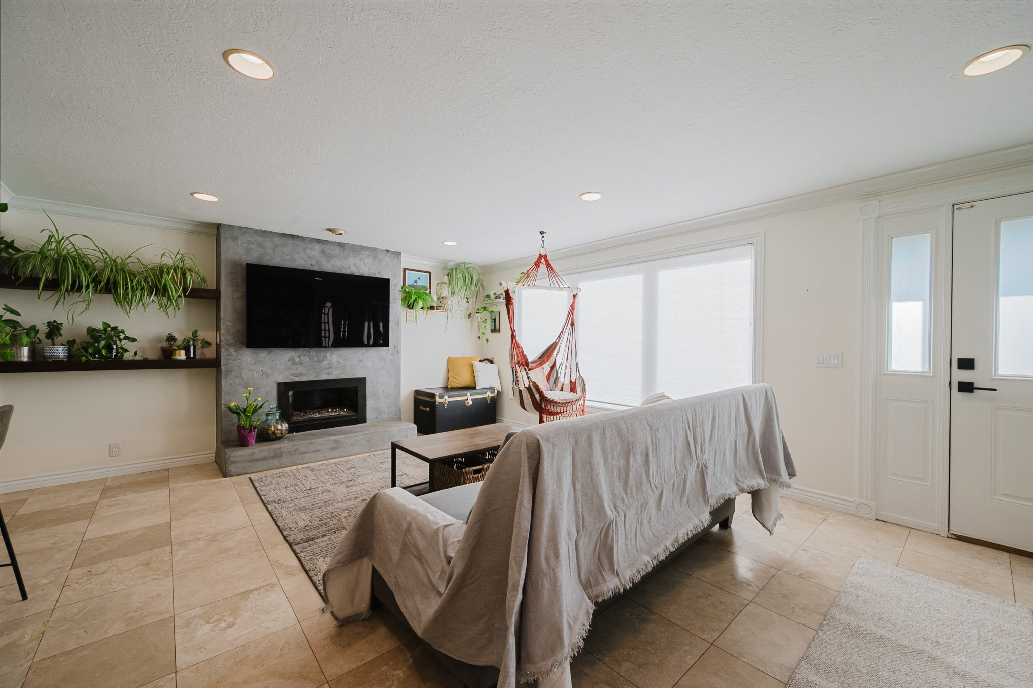 Living area with recessed ceiling lighting, a contemporary fireplace with a concrete-finish surround, and light-toned tile flooring