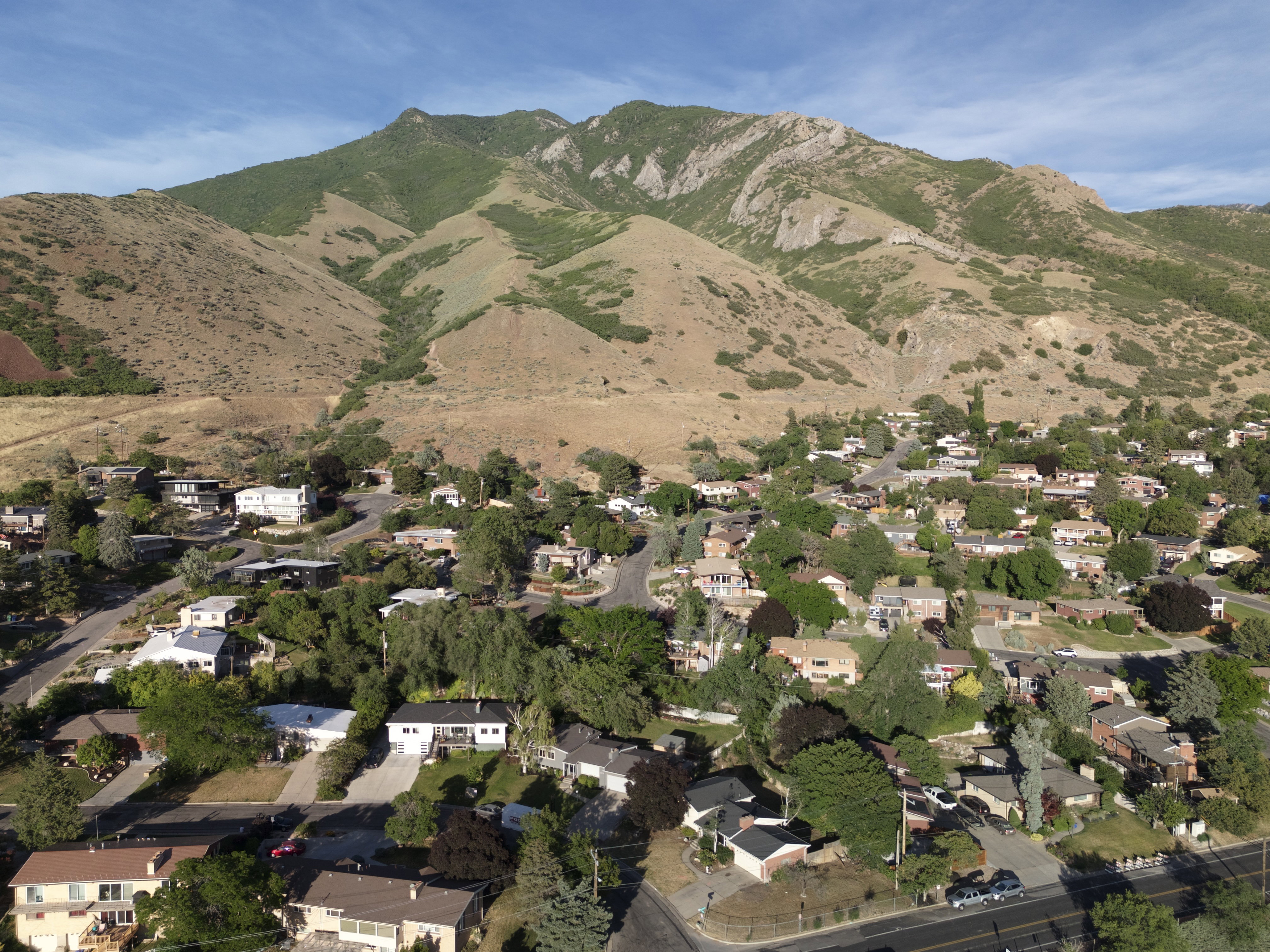 Residential area nestled at the base of a prominent mountain range, featuring a variety of homes with mature trees and paved roads