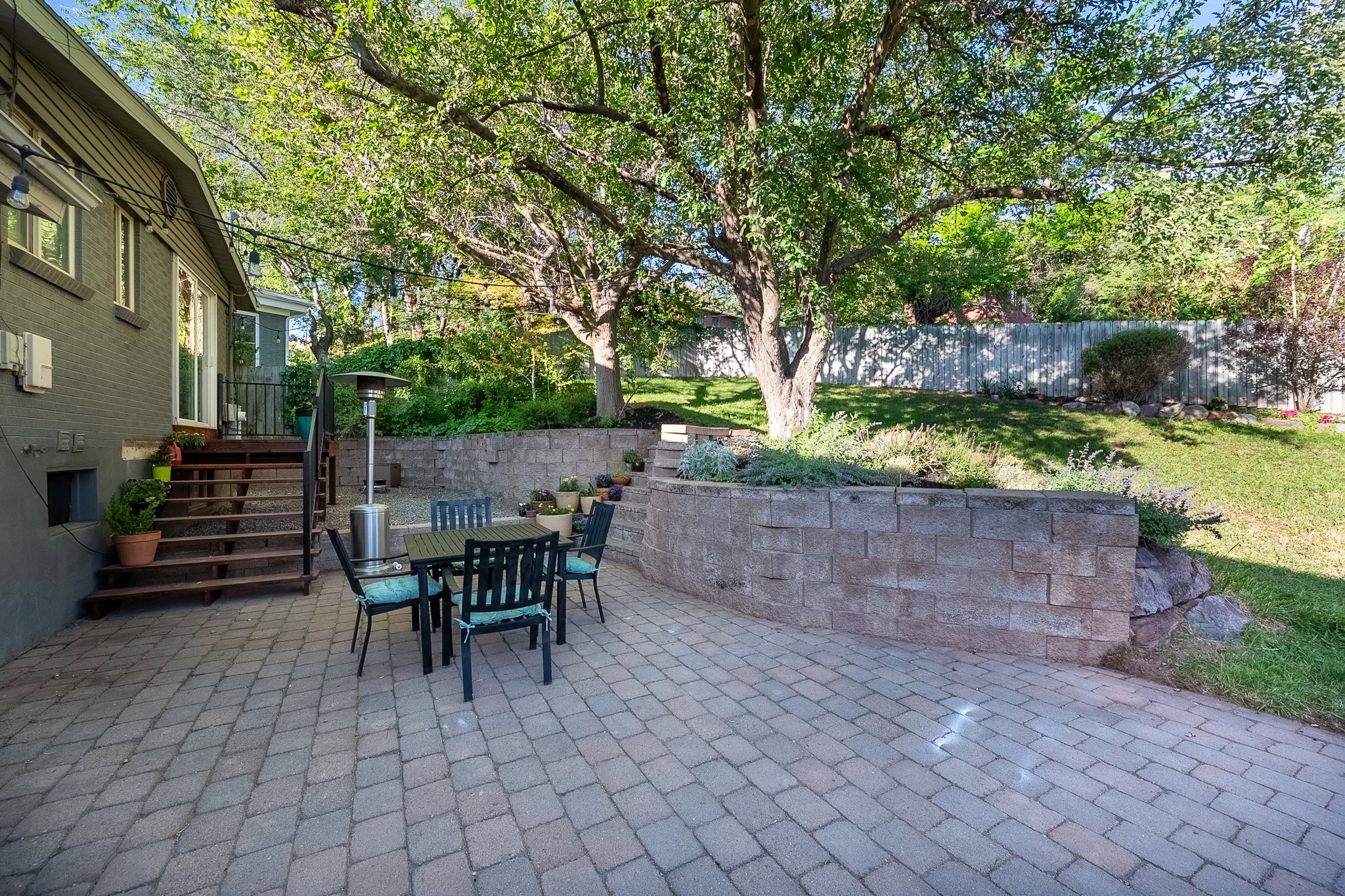 Expansive paver patio with a stone retaining wall and mature trees providing natural shade