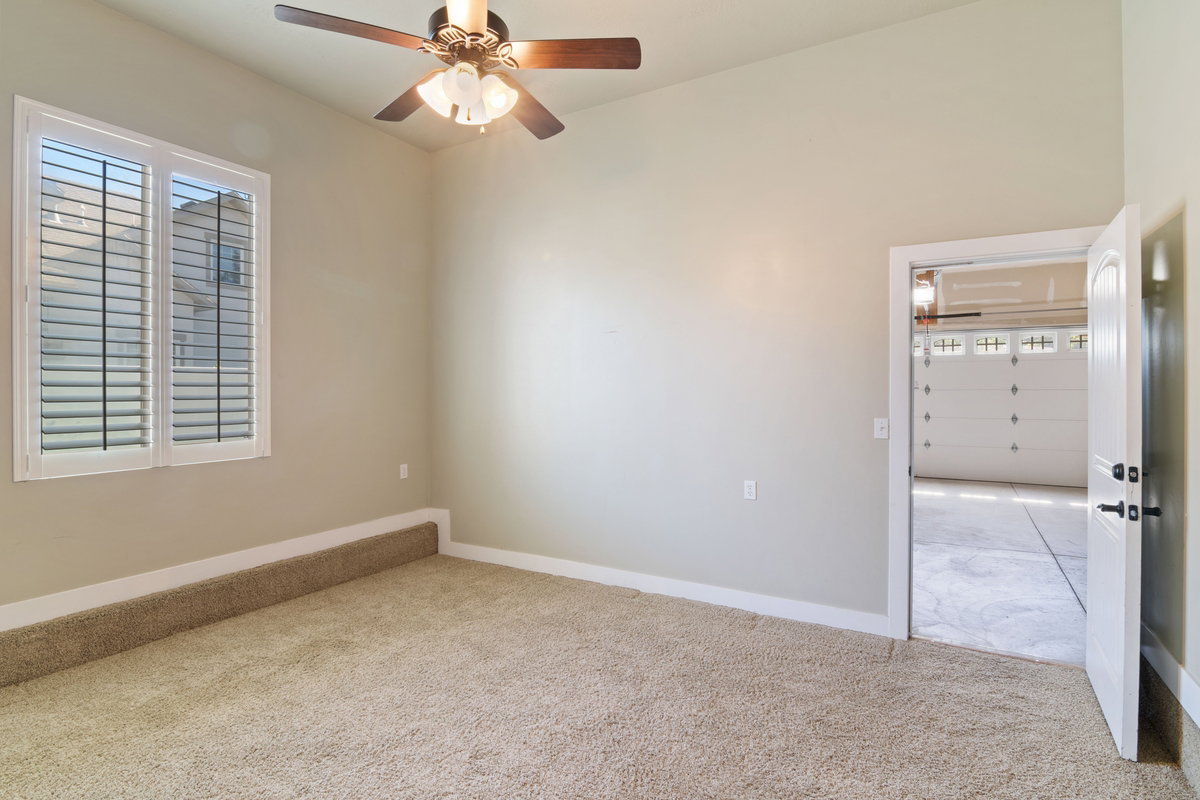 Carpeted interior space featuring a ceiling fan with light fixture, window with plantation shutters, light-toned walls, and white baseboards
