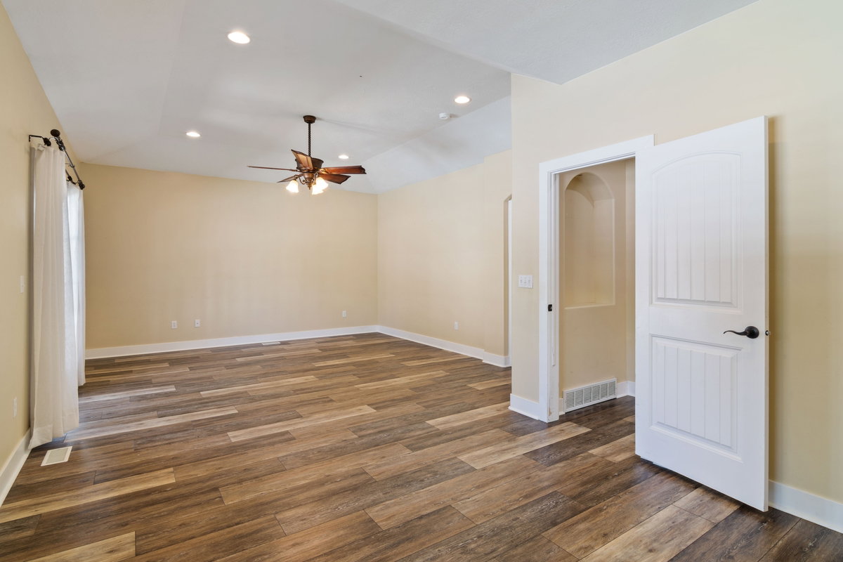 Spacious interior room featuring wood-finish flooring, vaulted ceiling with recessed lighting, and a ceiling fan
