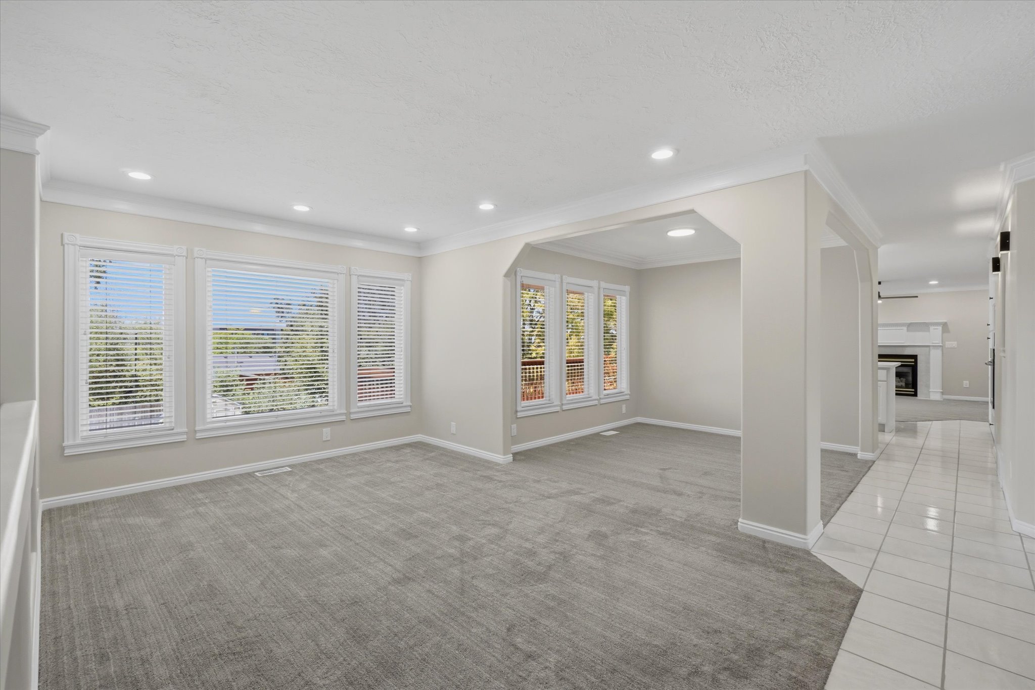 Expansive living area featuring large windows with louvered blinds, recessed lighting, crown molding, and neutral-toned carpeting
