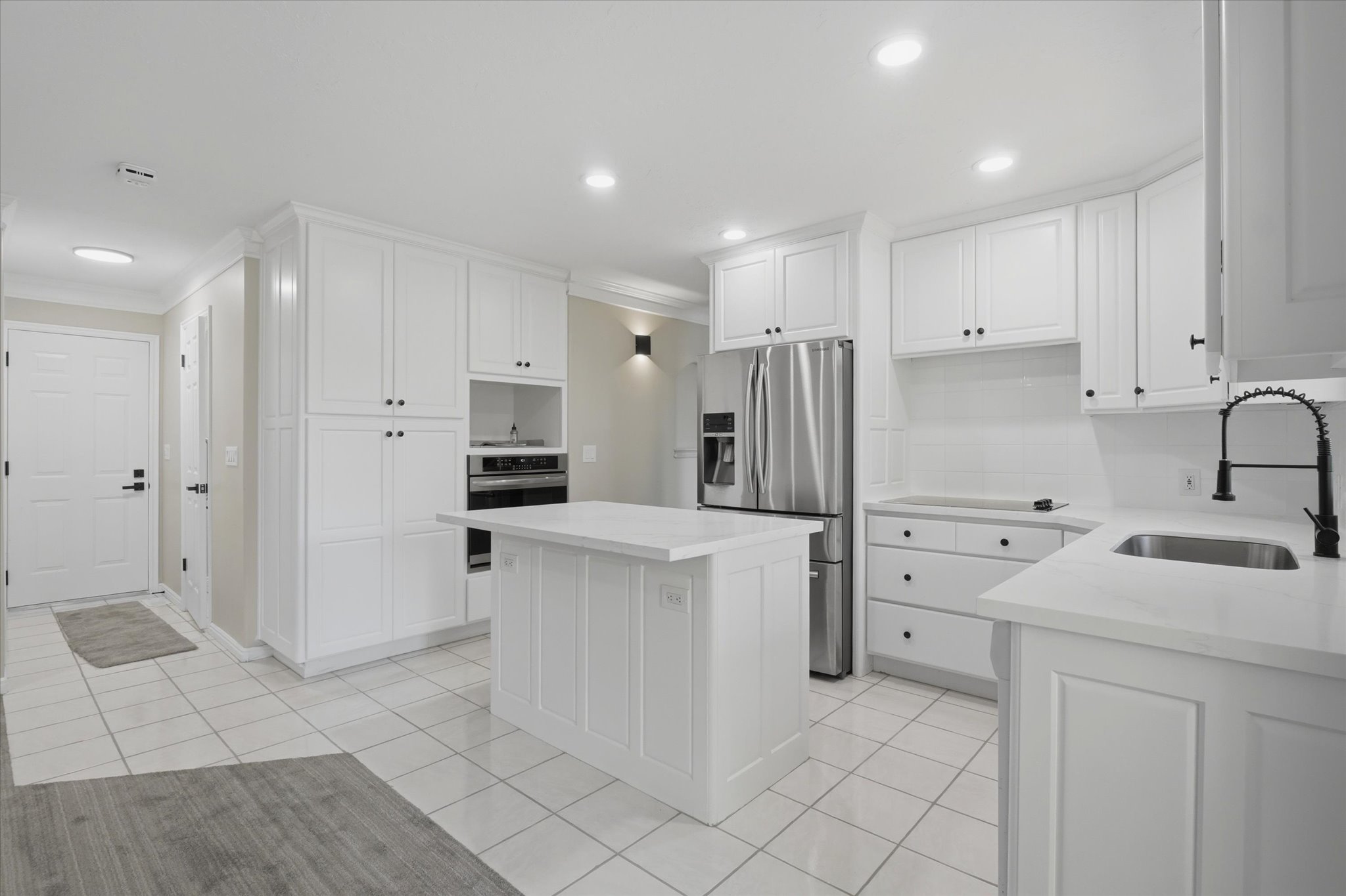 White kitchen featuring a central island, stainless steel refrigerator, built-in oven, white tile flooring, and white cabinetry