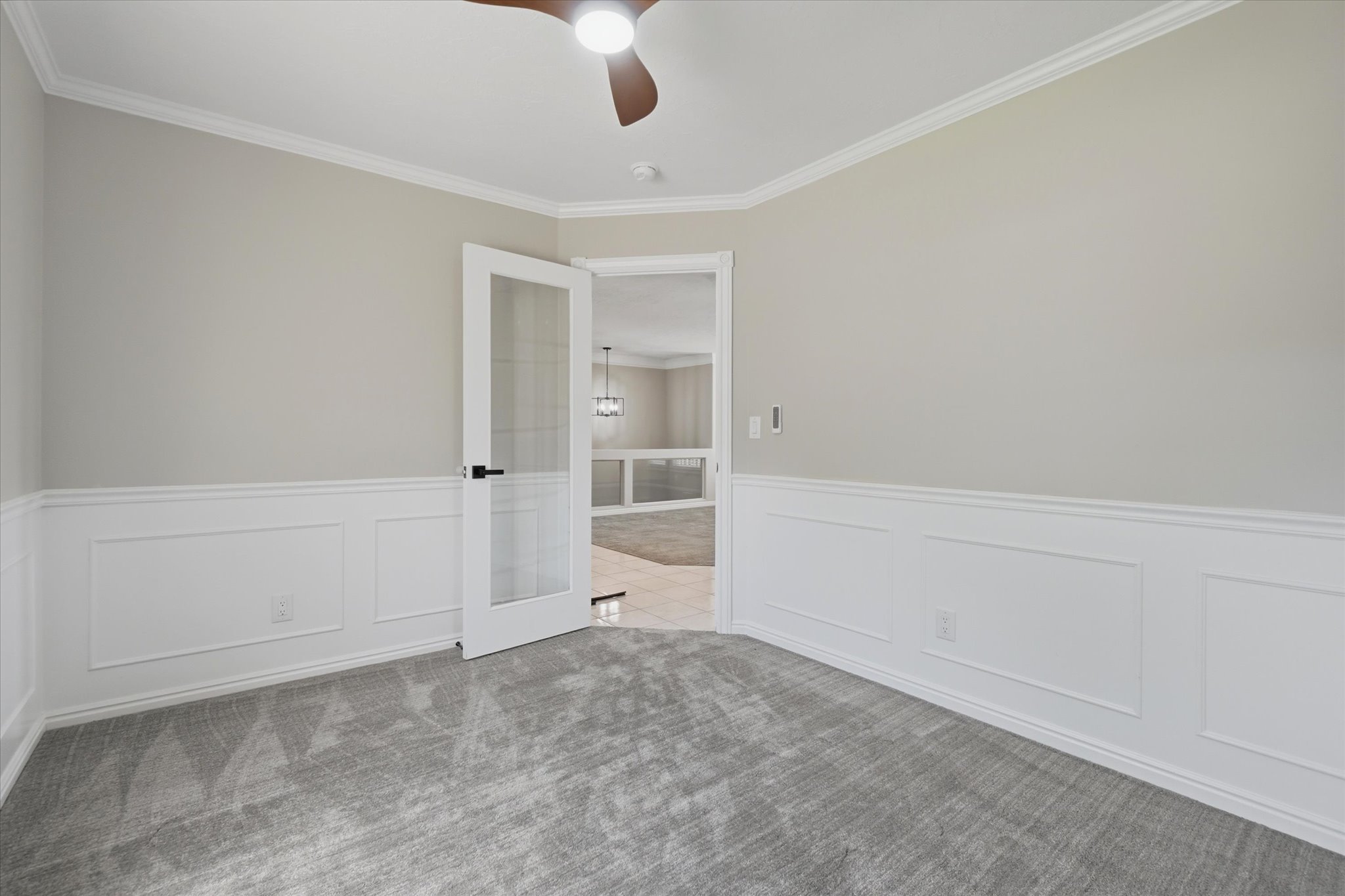 Interior room featuring wainscoting, crown molding, and a ceiling fan with integrated lighting