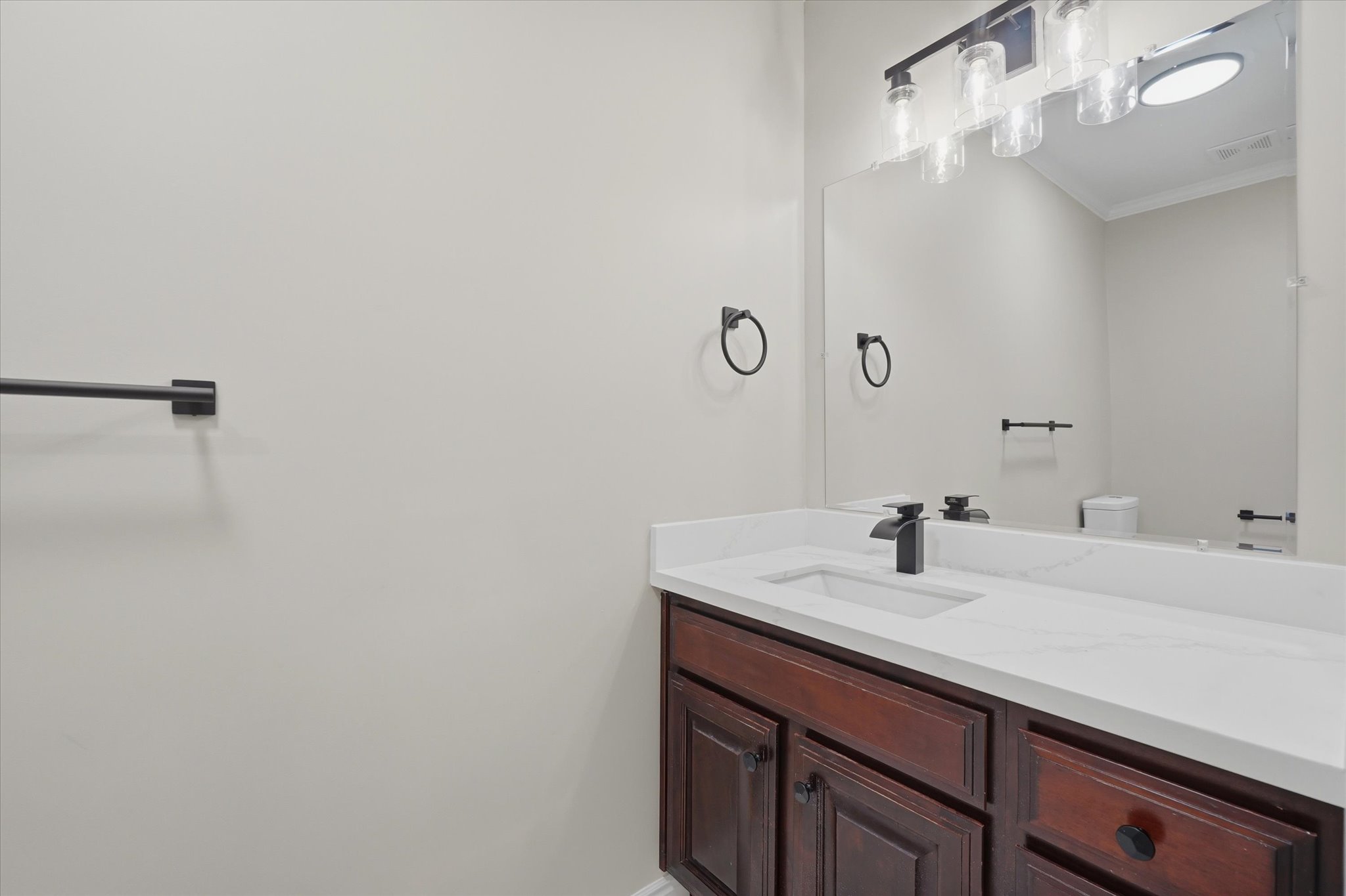Bathroom vanity featuring a rich wood-finish cabinet with black hardware, a pristine white countertop, and a sink