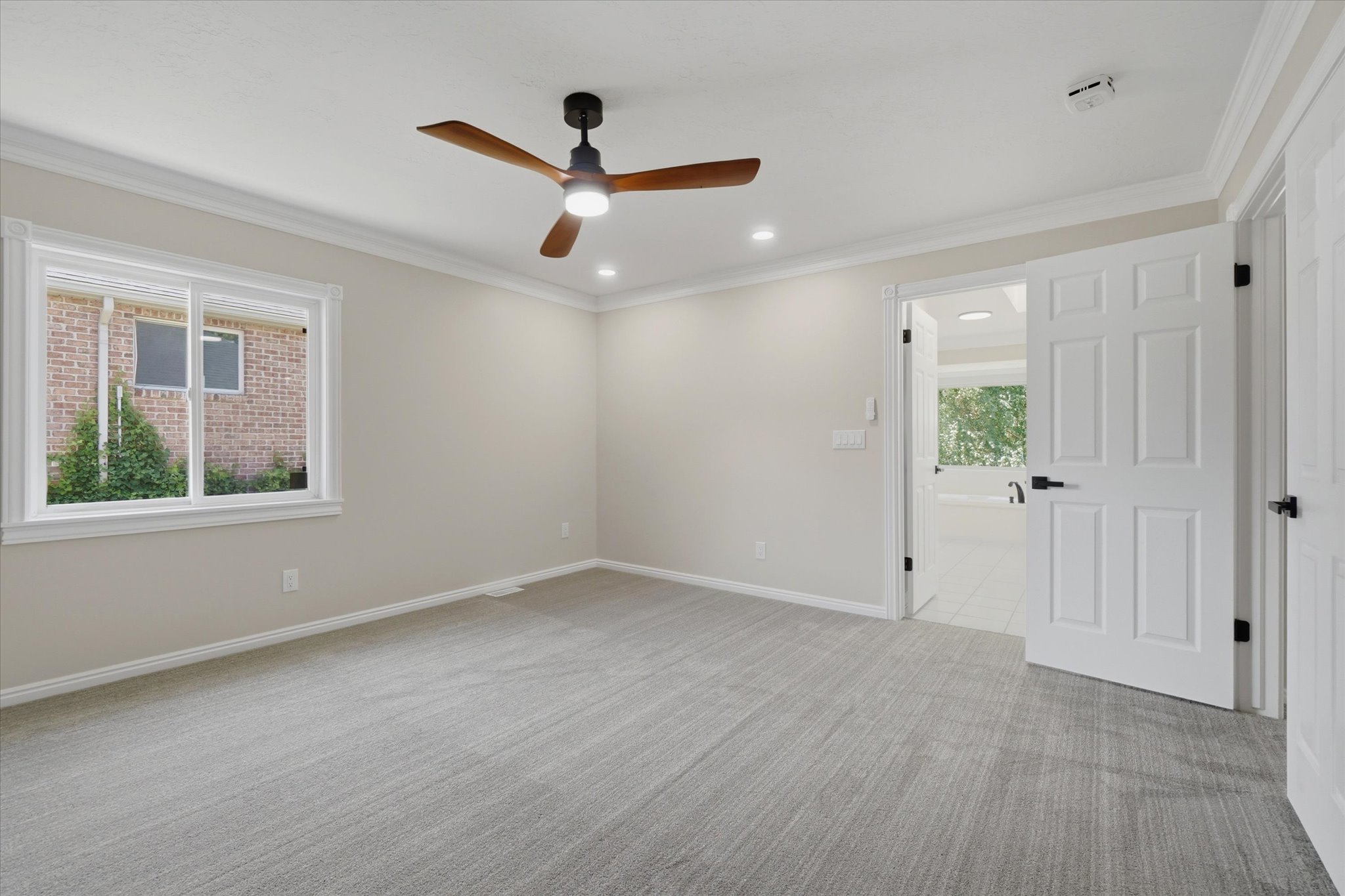 Spacious room featuring neutral carpet, crown molding, and a modern ceiling fan with integrated lighting