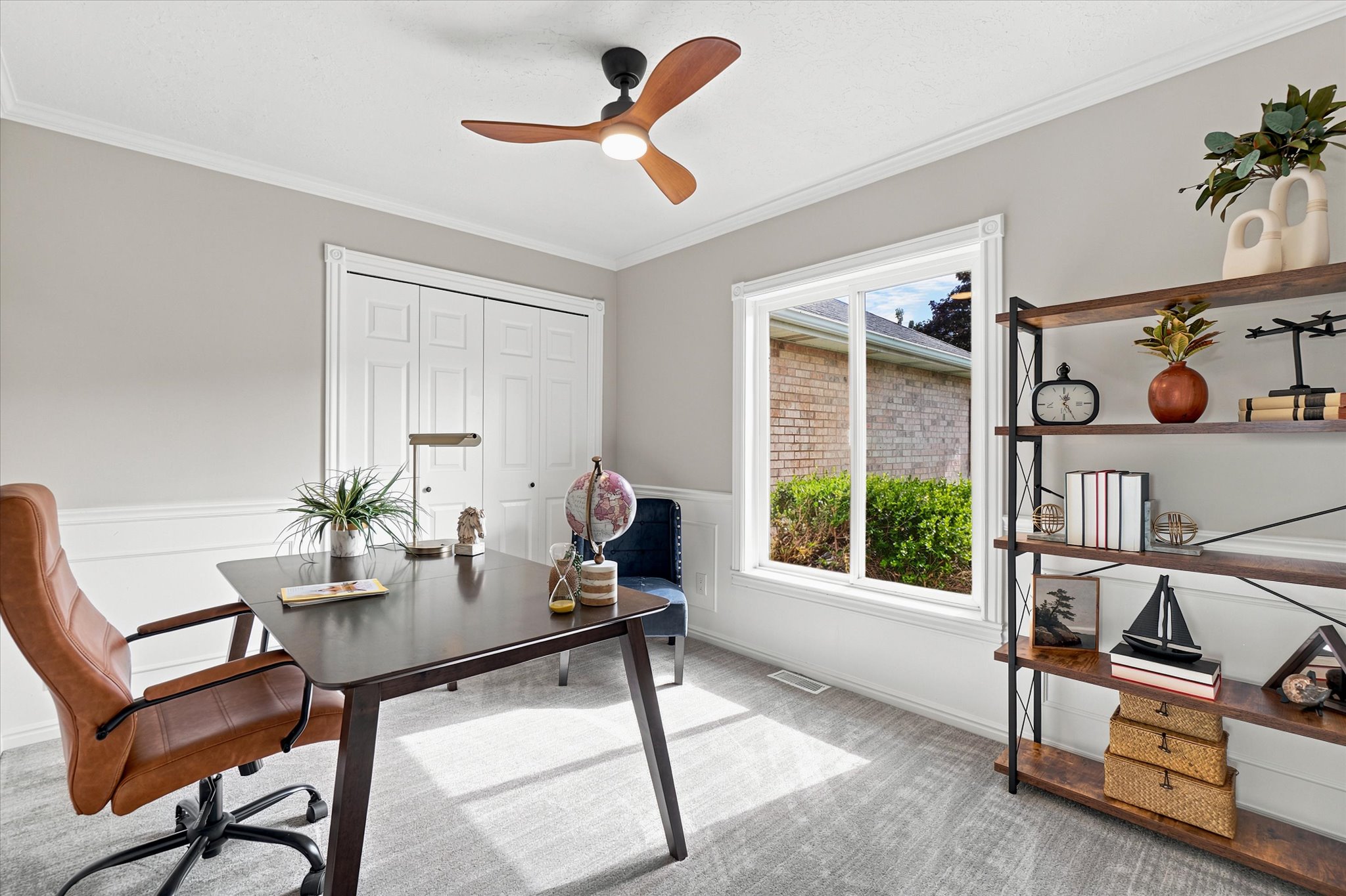 Office space featuring a ceiling fan with integrated lighting, a large window, bi-fold closet doors, white wainscoting, and crown molding - could be used as a bedroom if needed.