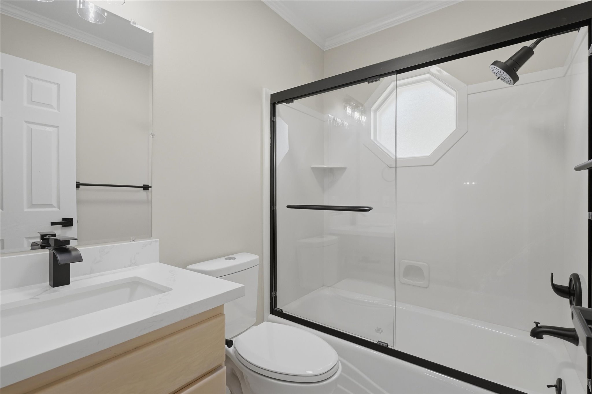 Bathroom featuring a tub/shower combination with black-framed glass enclosure, white octagon window, and matte black fixtures