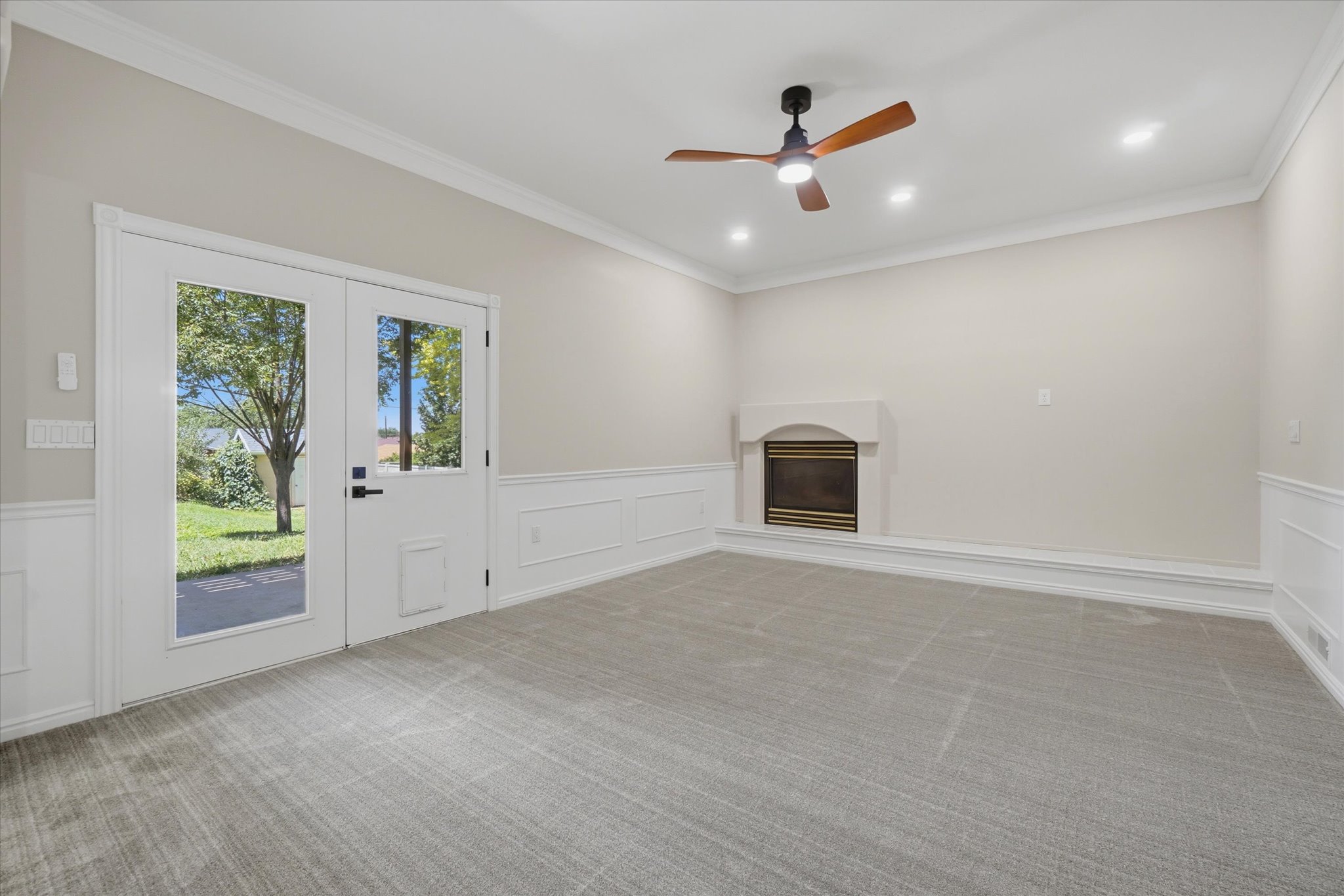 Spacious room featuring light gray carpeting, wainscoting, and crown molding