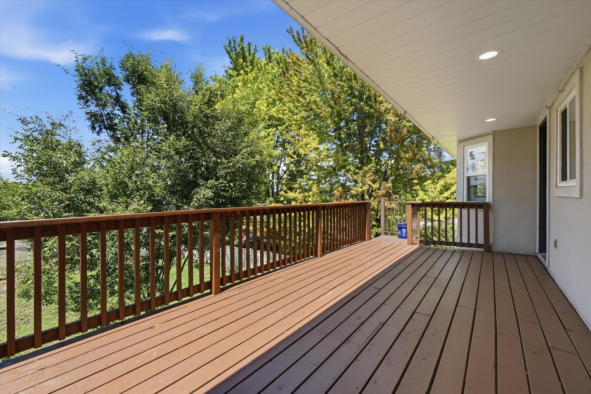 Expansive outdoor deck featuring wood-finish flooring, wood railings, and a covered ceiling with recessed lighting