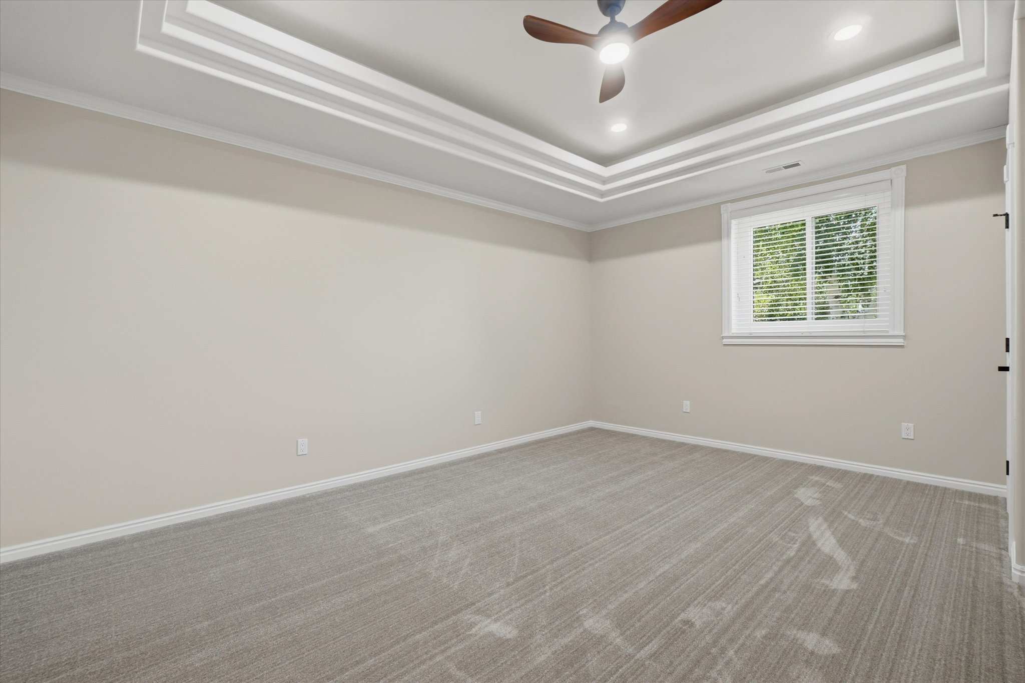 Neutral tone walls with white baseboards frame a spacious room featuring patterned carpeting