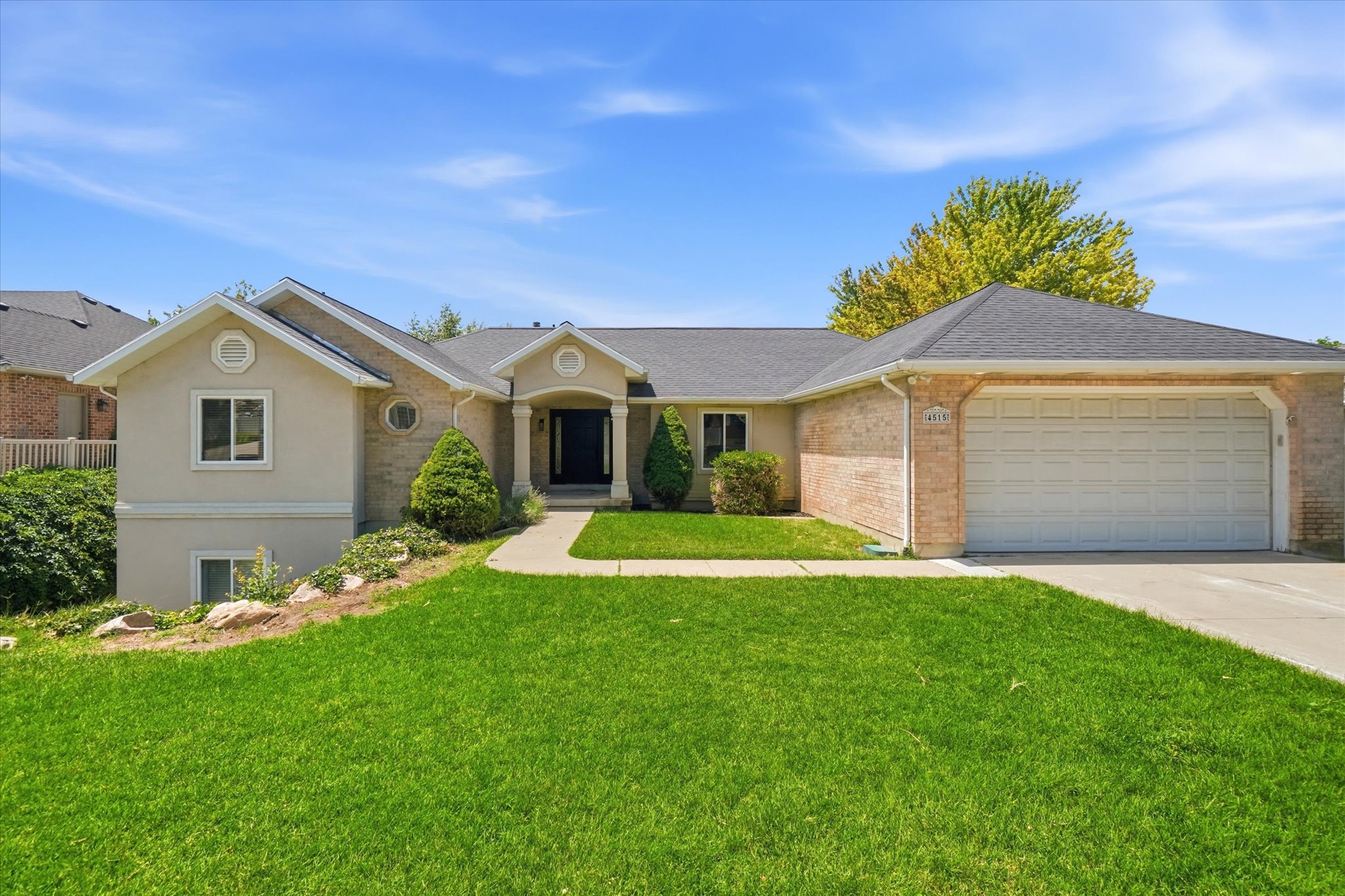 Spacious ranch-style residence featuring a two-car garage, brick and stucco exterior, And front lawn with mature landscaping