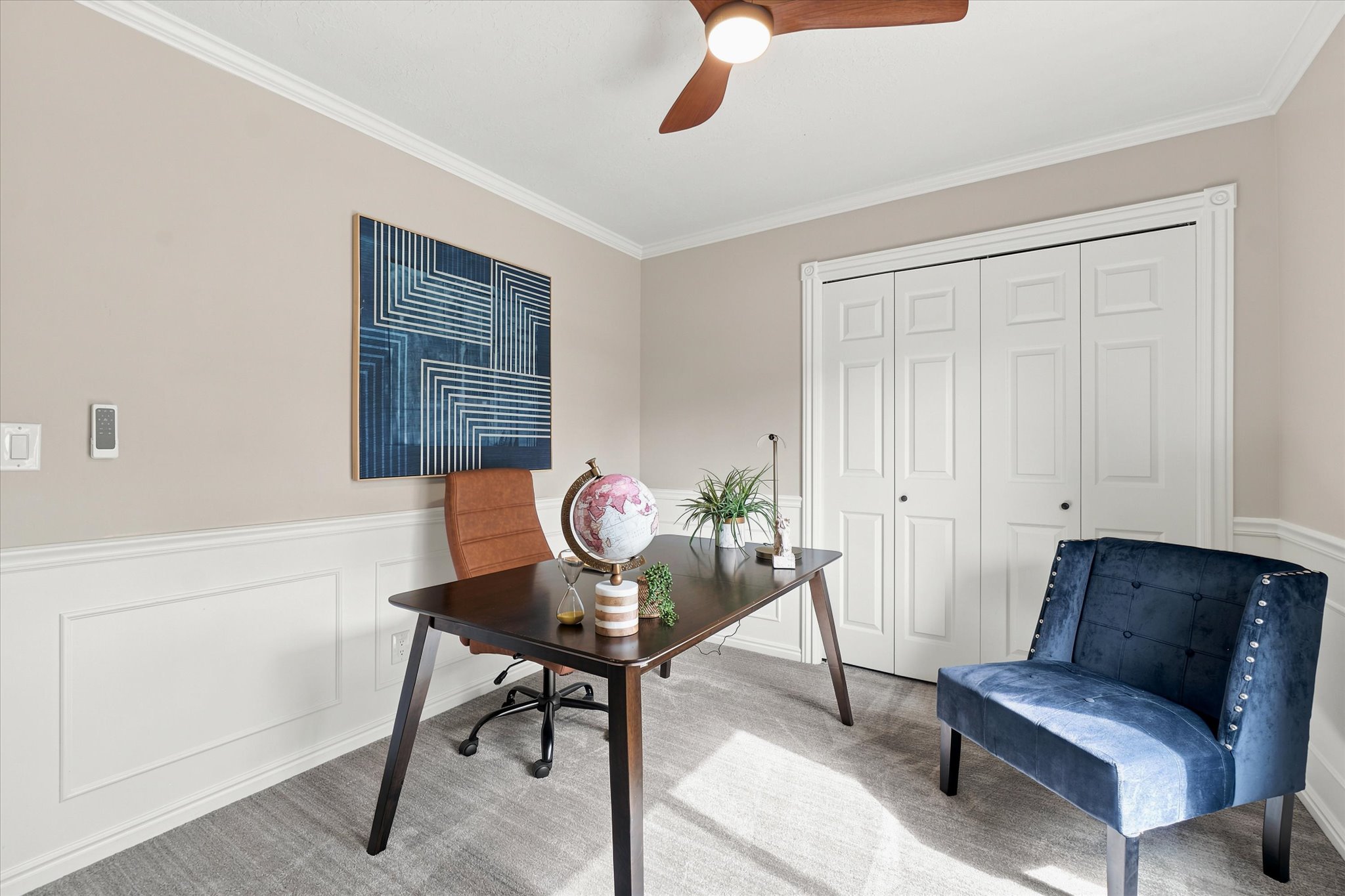 Carpeted room featuring wainscoting, crown molding, and a ceiling fan.  this room is just off of the front entry, making it a good place for meeting guests or transacting business.