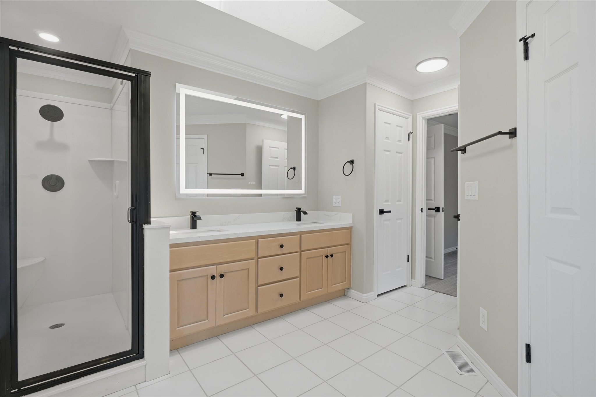 Bathroom featuring a dual vanity with light wood cabinetry, white countertops, and matte black fixtures