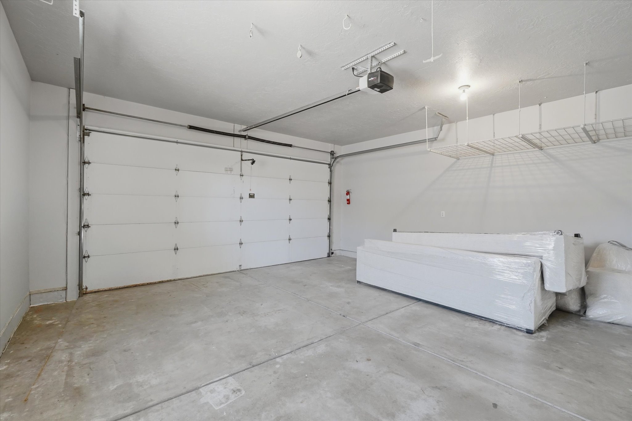 Spacious garage featuring a concrete floor, white panel garage door, and an automatic garage door opener and storage above.
