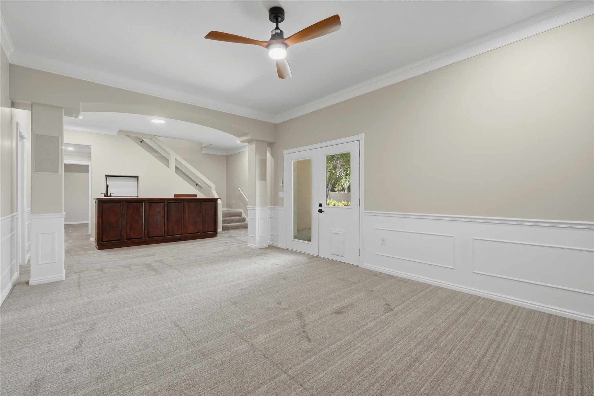 Spacious room featuring light-toned carpeting, wainscoting, and crown molding