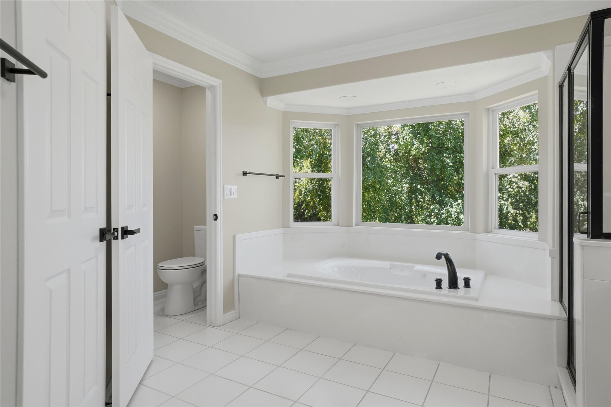 Soaking tub set within a bay window, featuring a black faucet and surrounded by white tile