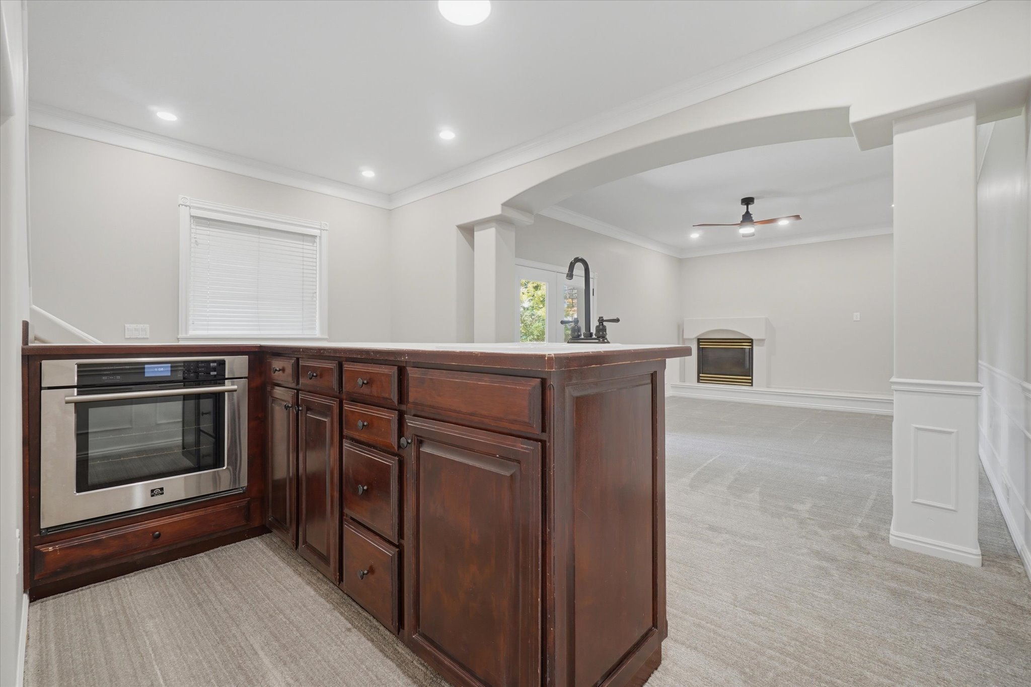 Kitchenette featuring built-in stainless steel oven, dark wood cabinetry with a light-toned countertop, and a matte black gooseneck faucet