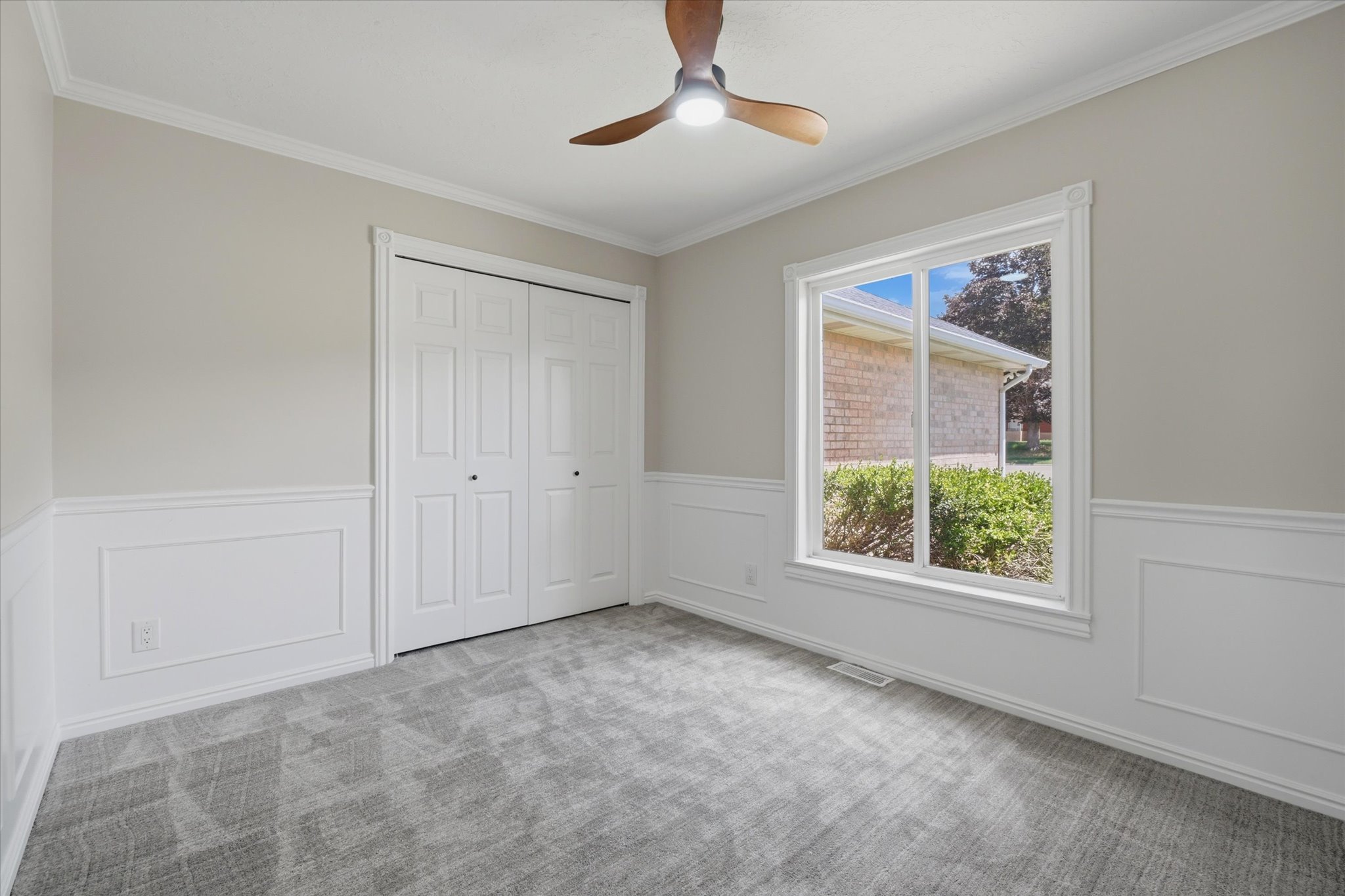 Interior room featuring a ceiling fan with integrated lighting, a large window with white trim, and a double-door closet.  Could be used as an office or bedroom.