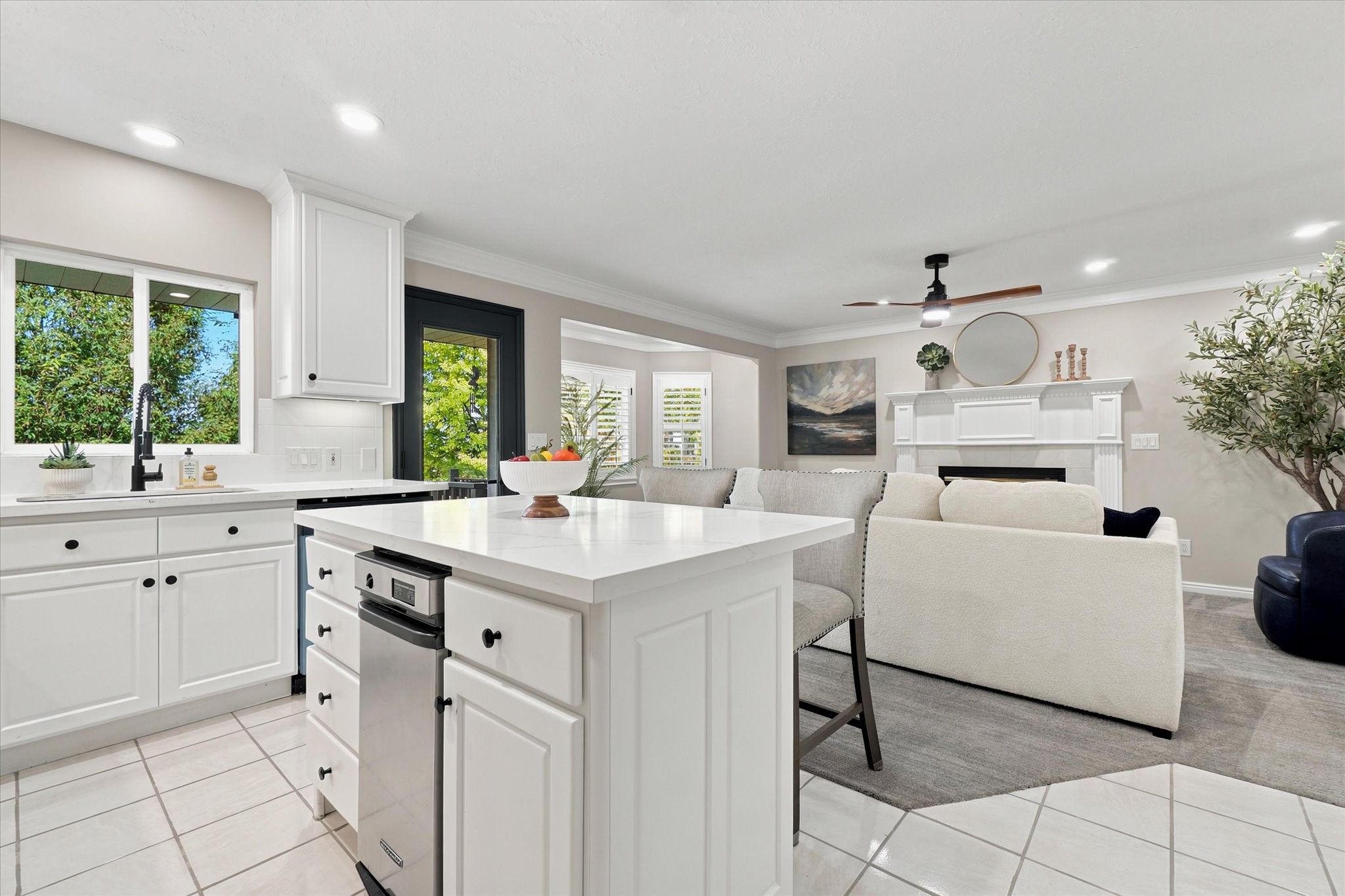 Open-concept kitchen and living area featuring white cabinetry, a kitchen island with integrated dishwasher, and a fireplace with a detailed mantel