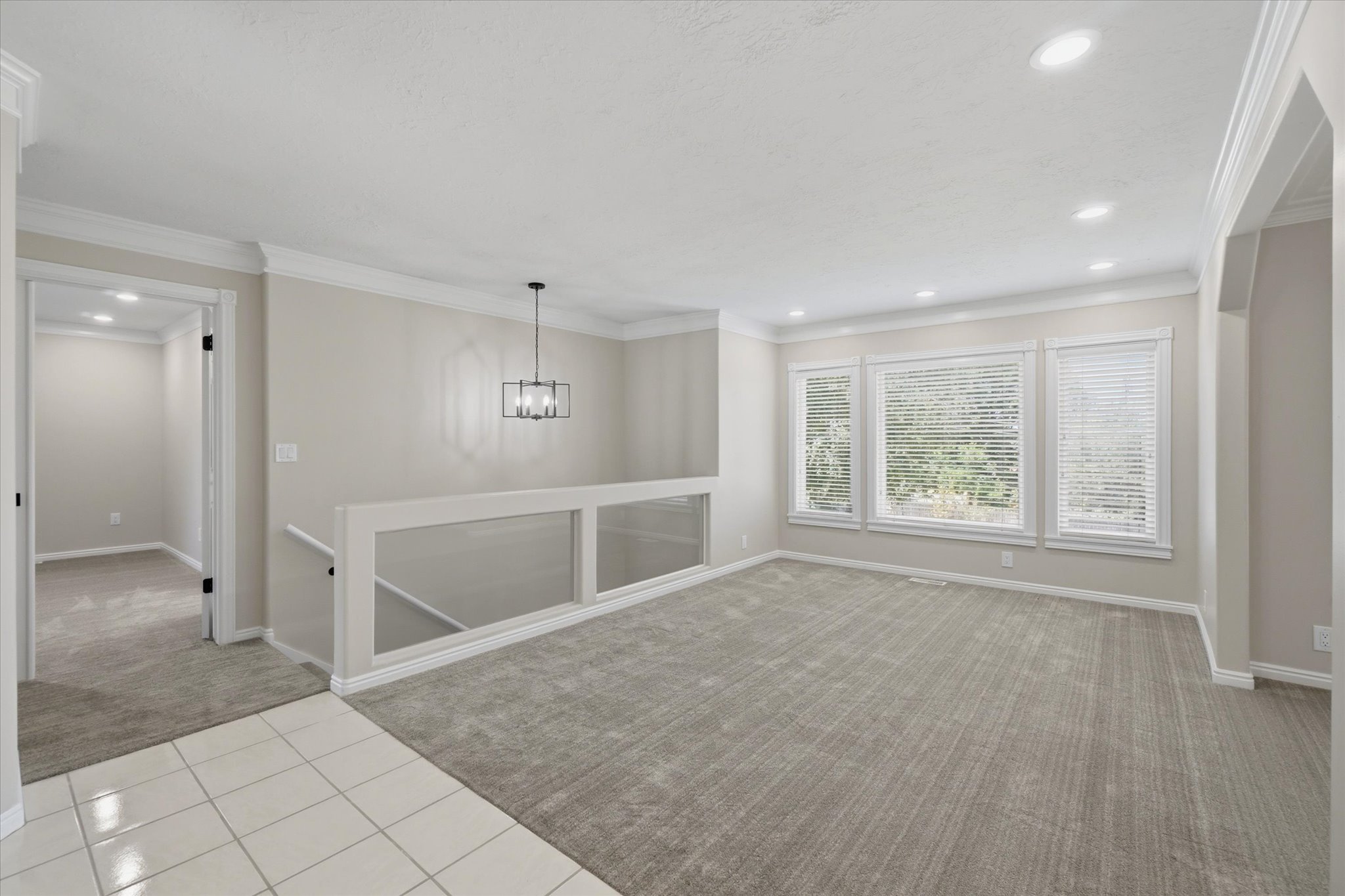 Spacious interior featuring a light gray carpet, white tile flooring, and a contemporary chandelier