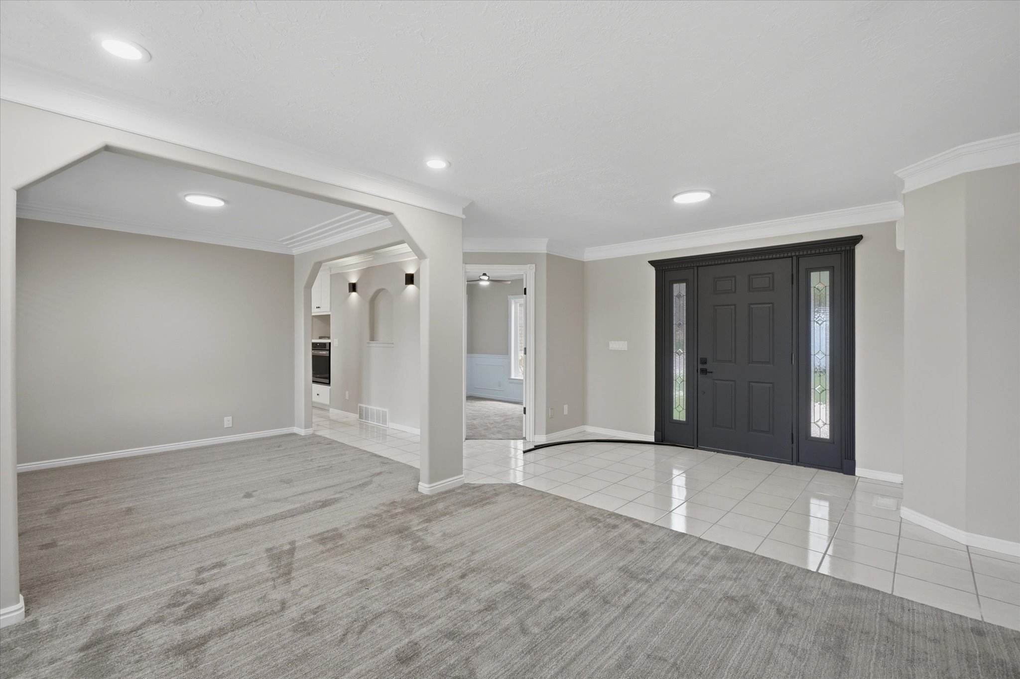 Entry foyer featuring a dark-paneled front door with sidelight windows, white tile flooring, and contrasting gray carpet